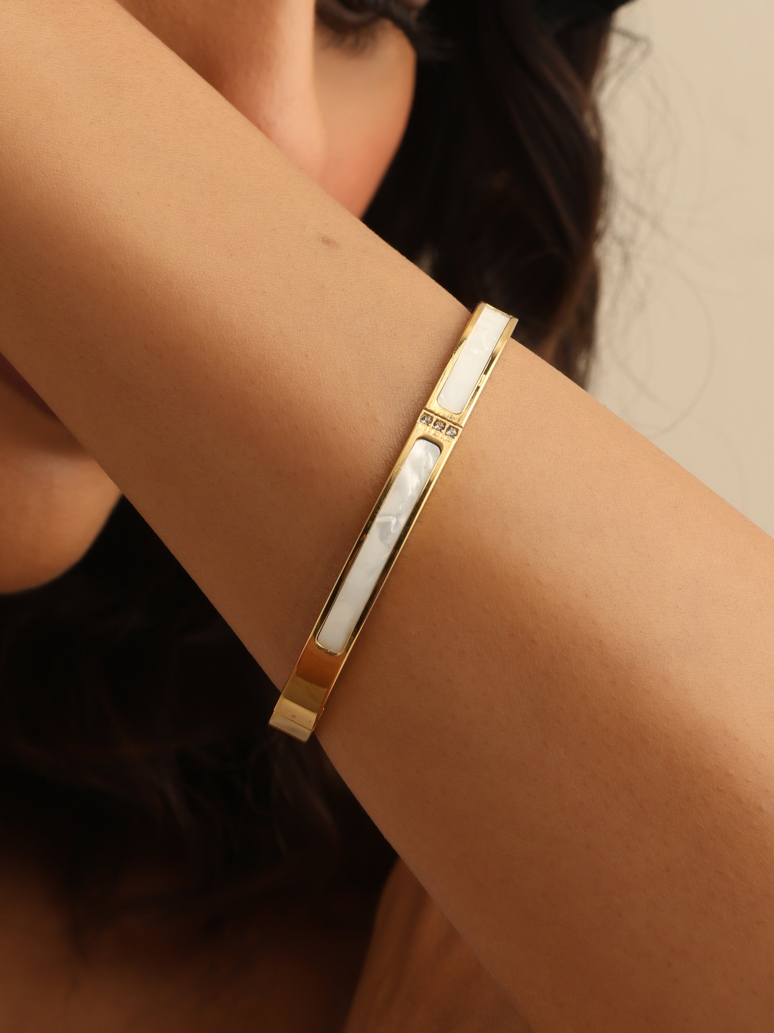 Close-up of a person wearing a gold bracelet on a neutral background