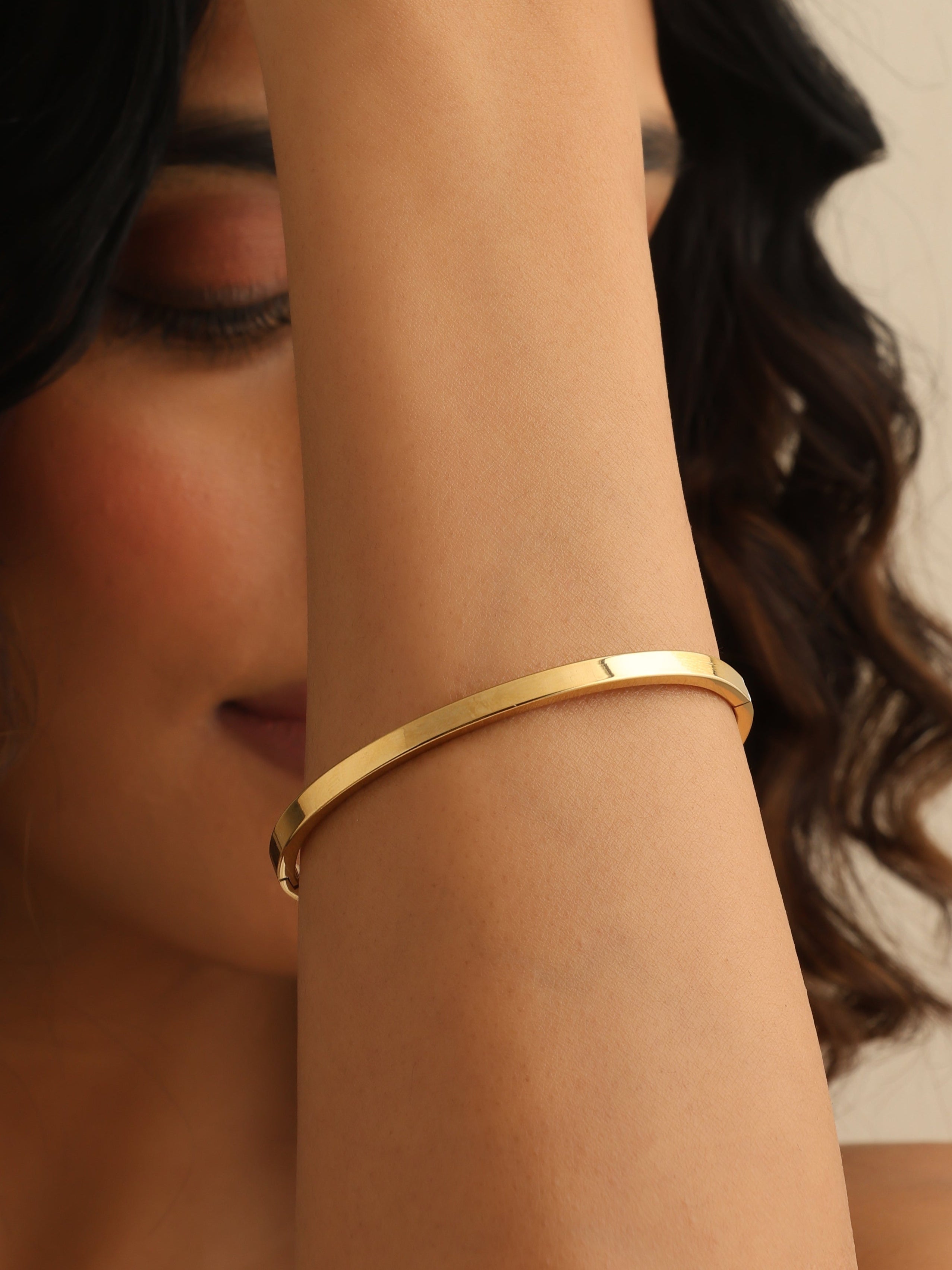 Close-up of a person wearing a gold bracelet with a neutral background
