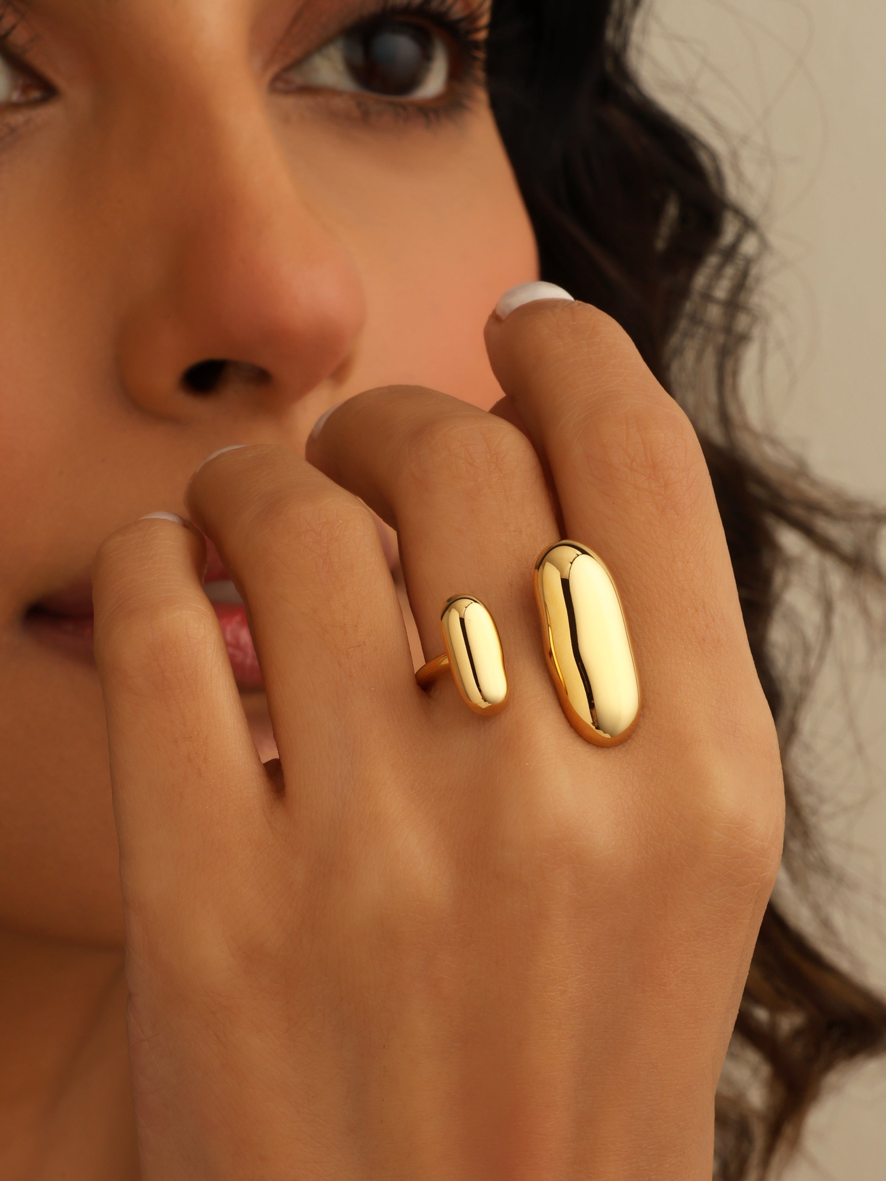 Close-up of a woman's hand wearing two gold rings with a neutral background