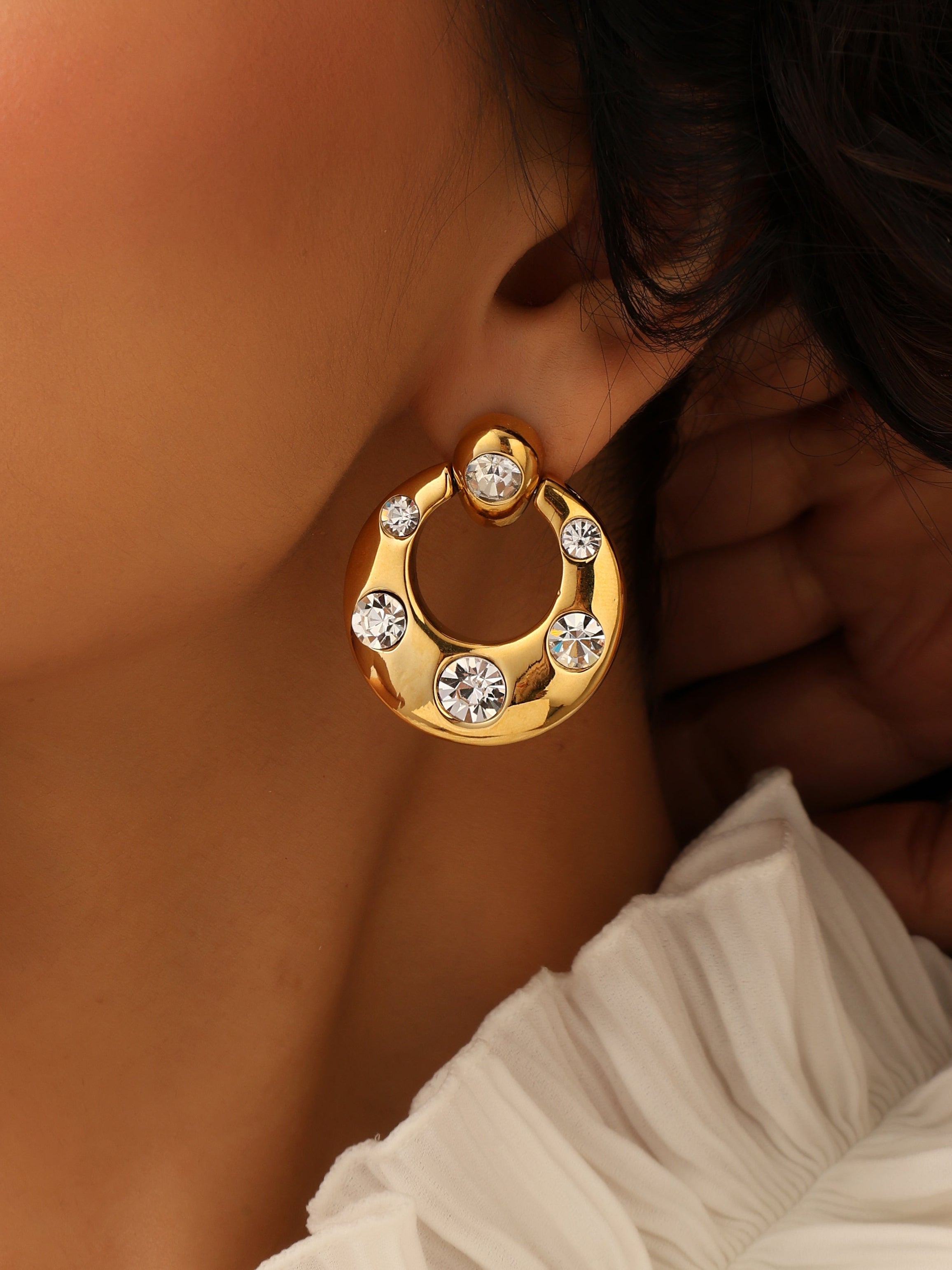 Gold hoop earring with embedded stones worn by a person