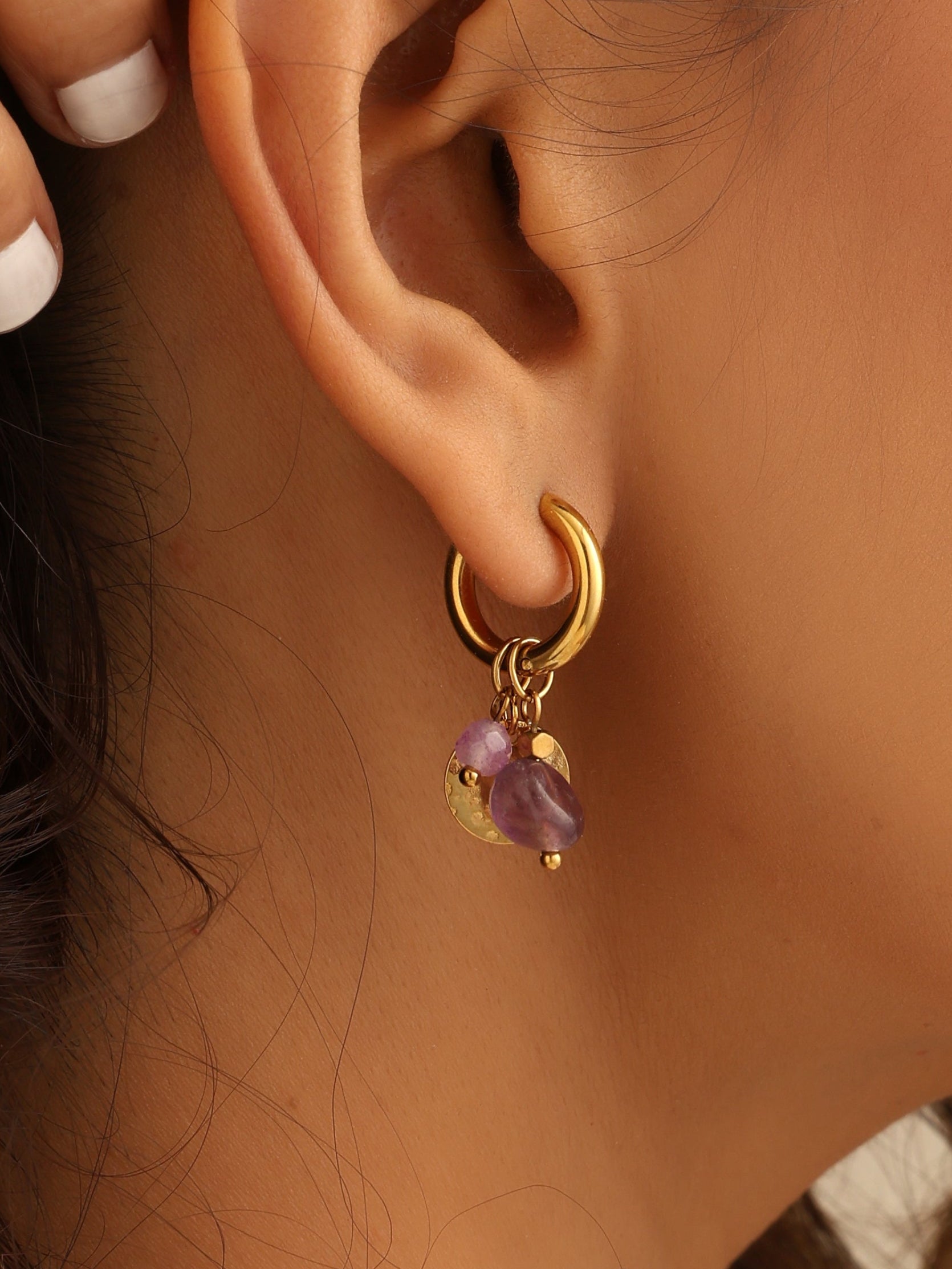 Close-up of an ear wearing a gold earring with purple gemstones.
