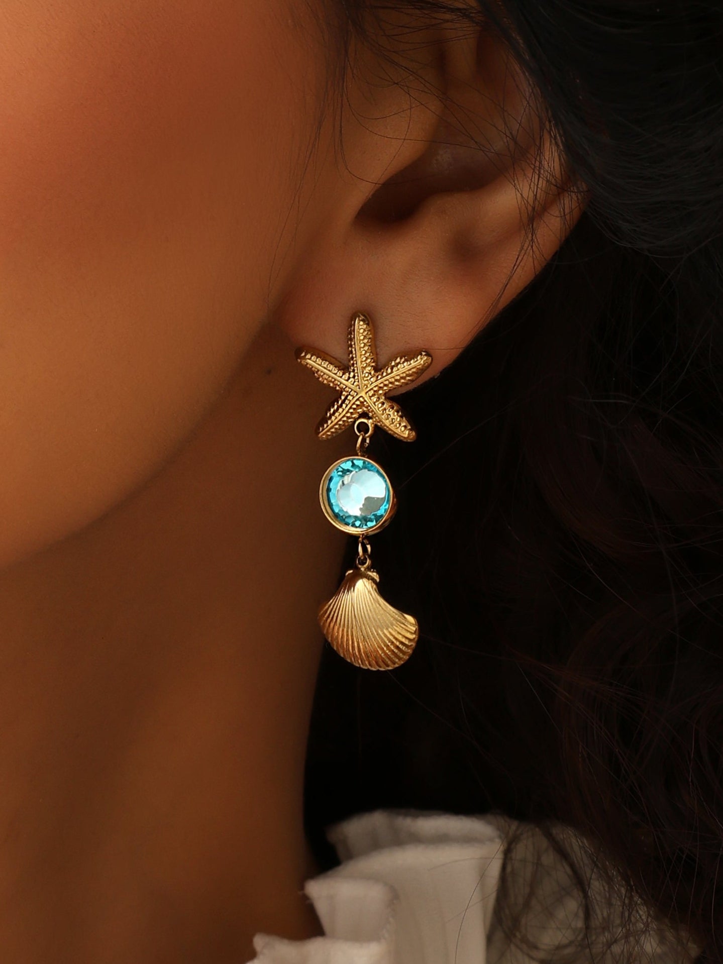 Close-up of a person wearing a starfish and shell earring with a blue gemstone.