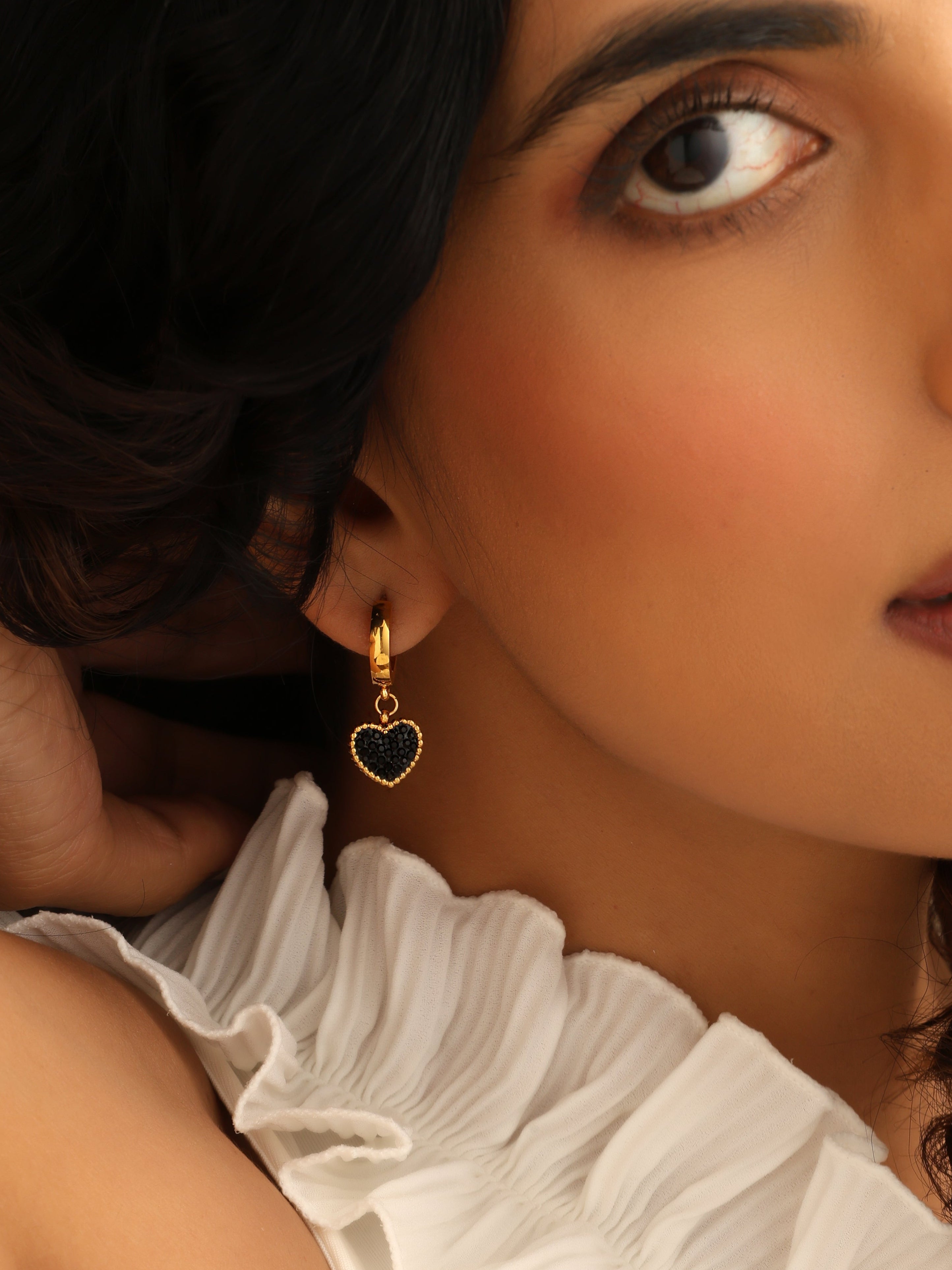 Close-up of a woman wearing a white ruffled top and gold earrings with a heart design.