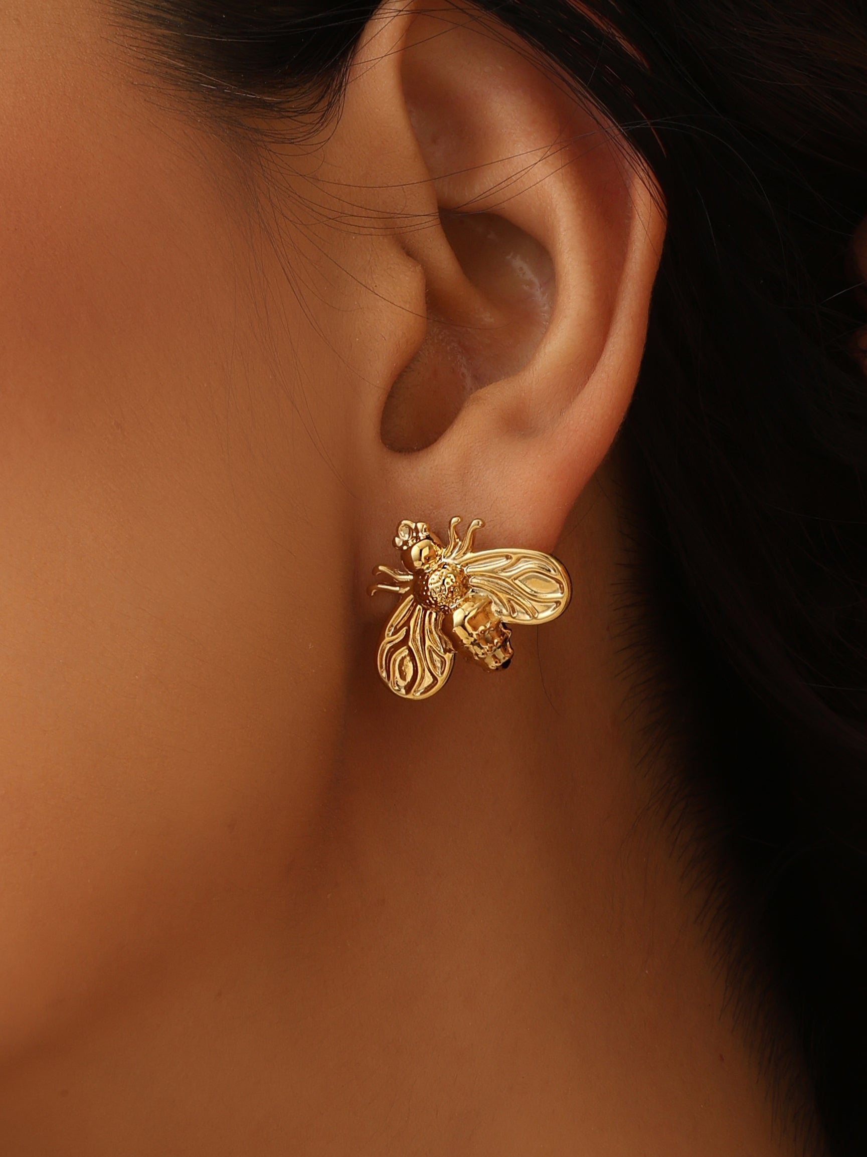 Gold bee-shaped earring worn by a person with dark hair.