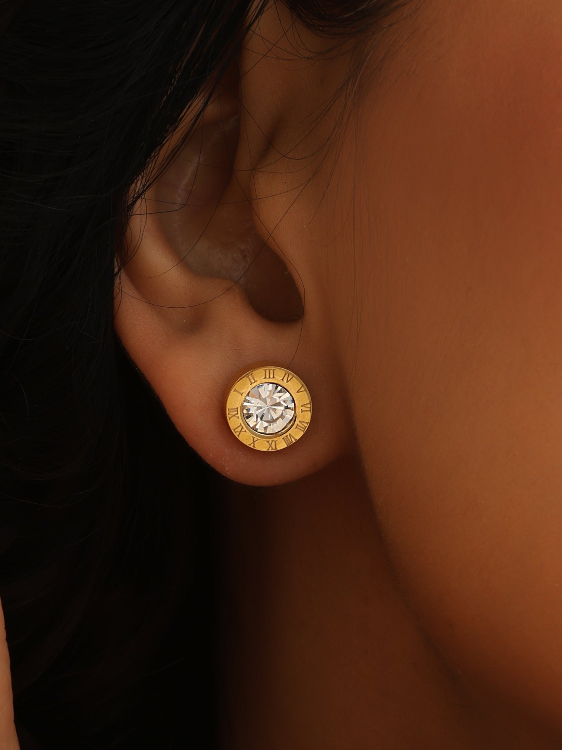 Close-up of a person wearing gold earrings with a dark background
