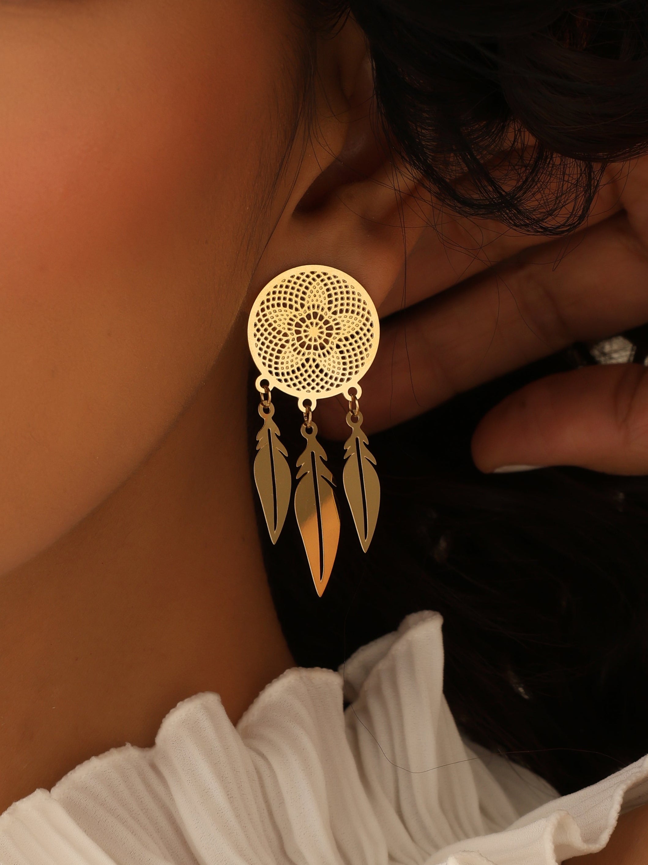 Gold dreamcatcher earring worn by a person with a white blouse.