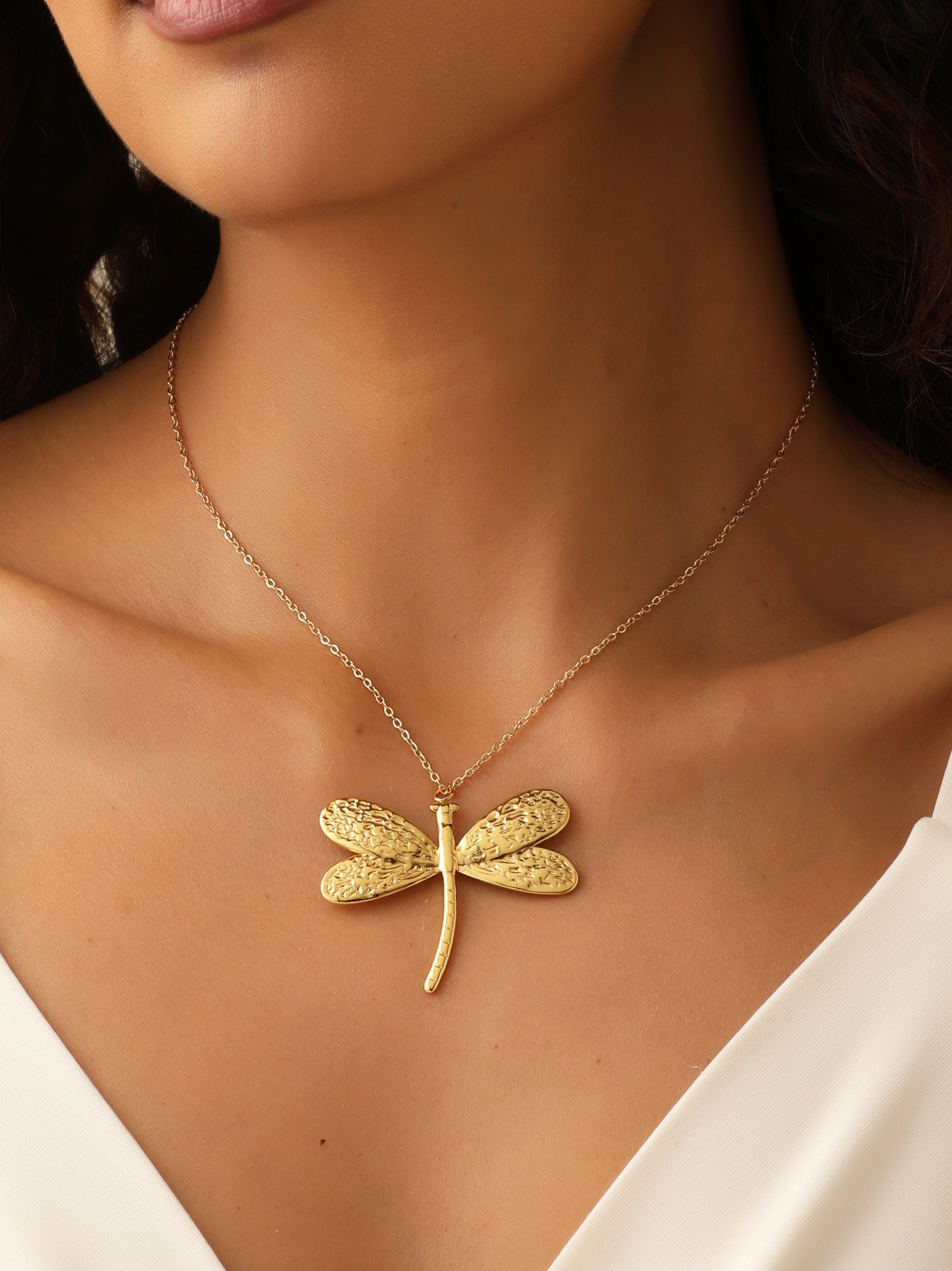Gold dragonfly necklace on a model wearing a white top