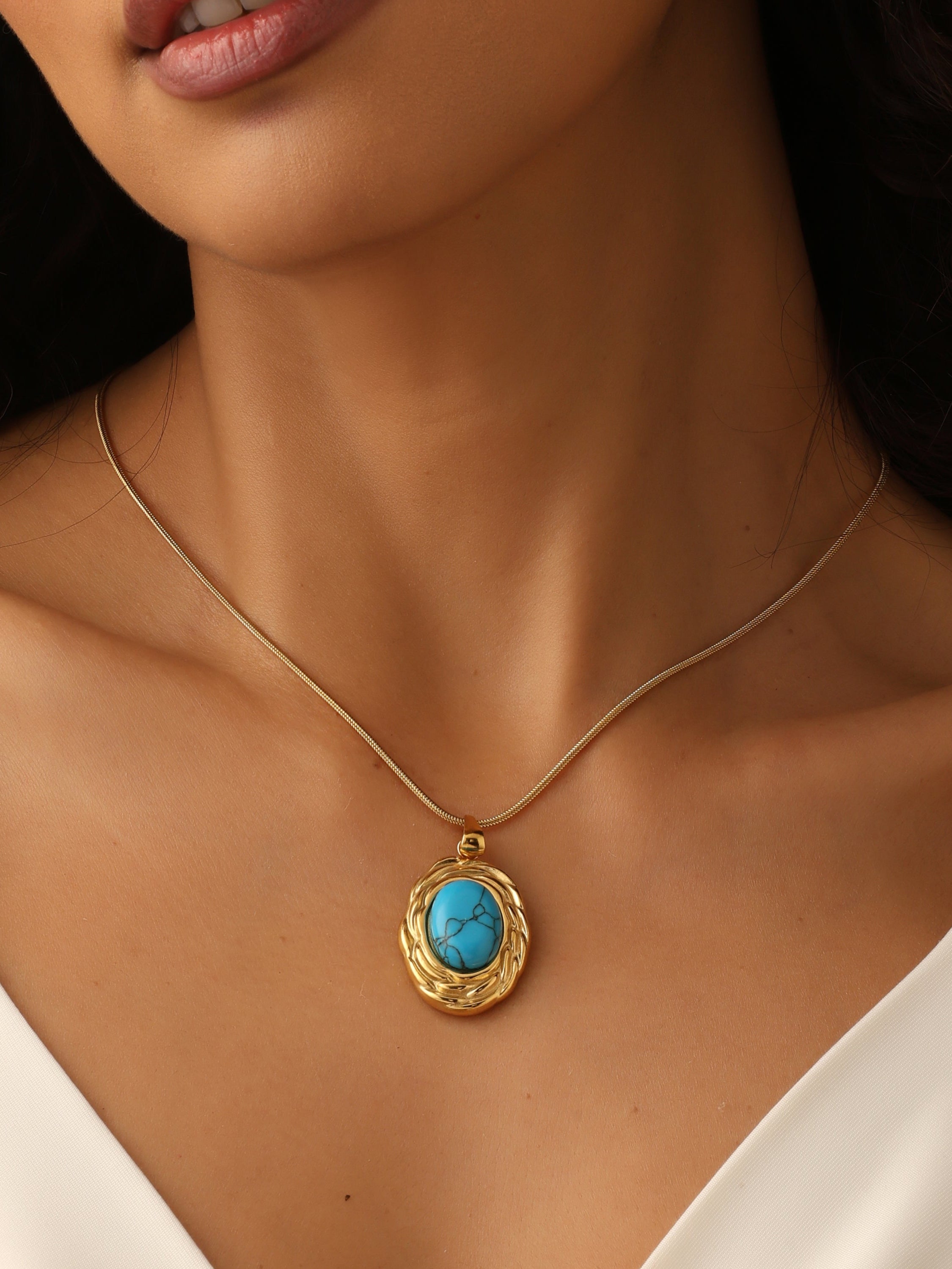 Close-up of a woman wearing a gold necklace with a turquoise pendant.