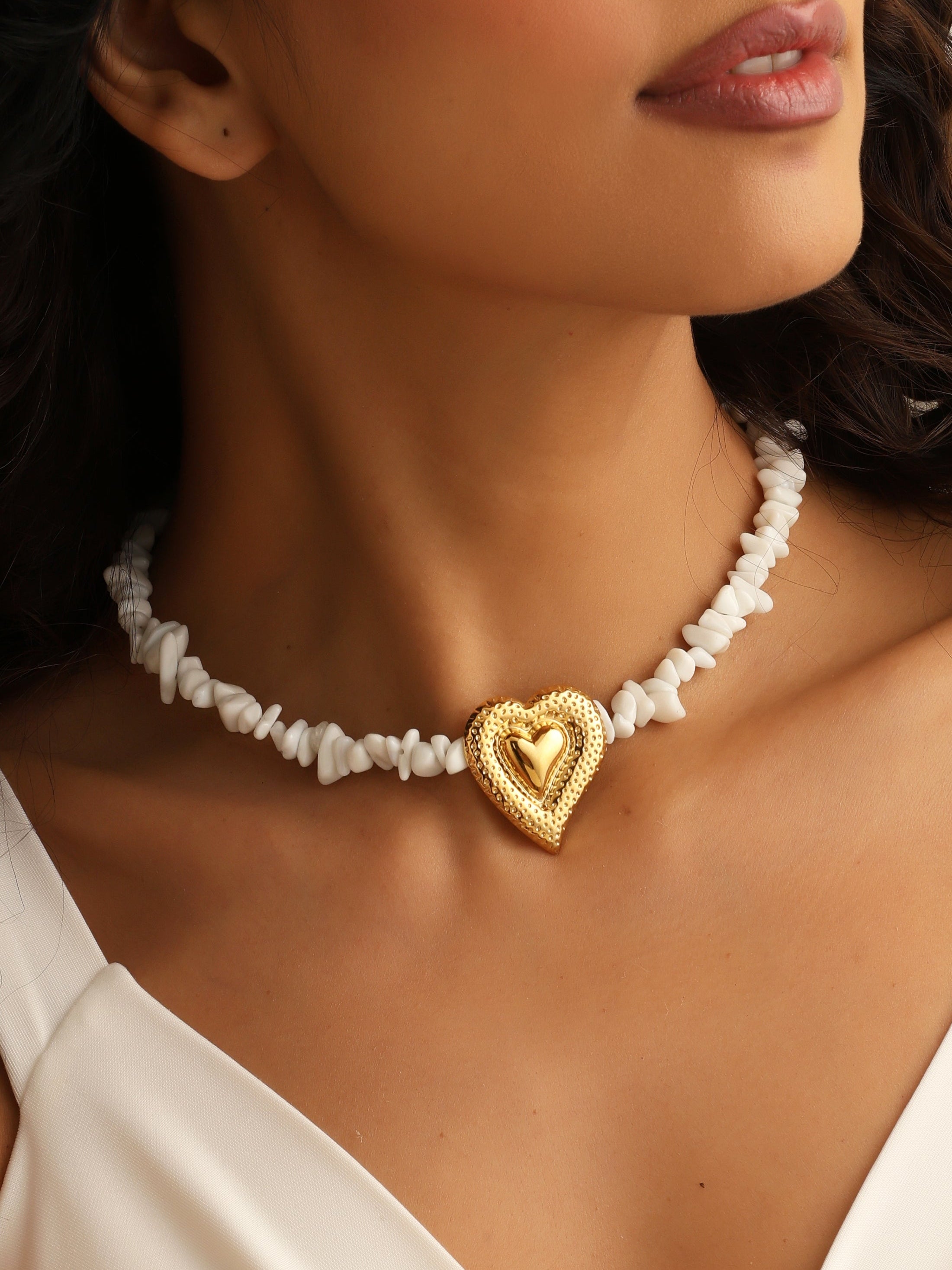 Woman wearing a gold heart-shaped pendant necklace with white beads.