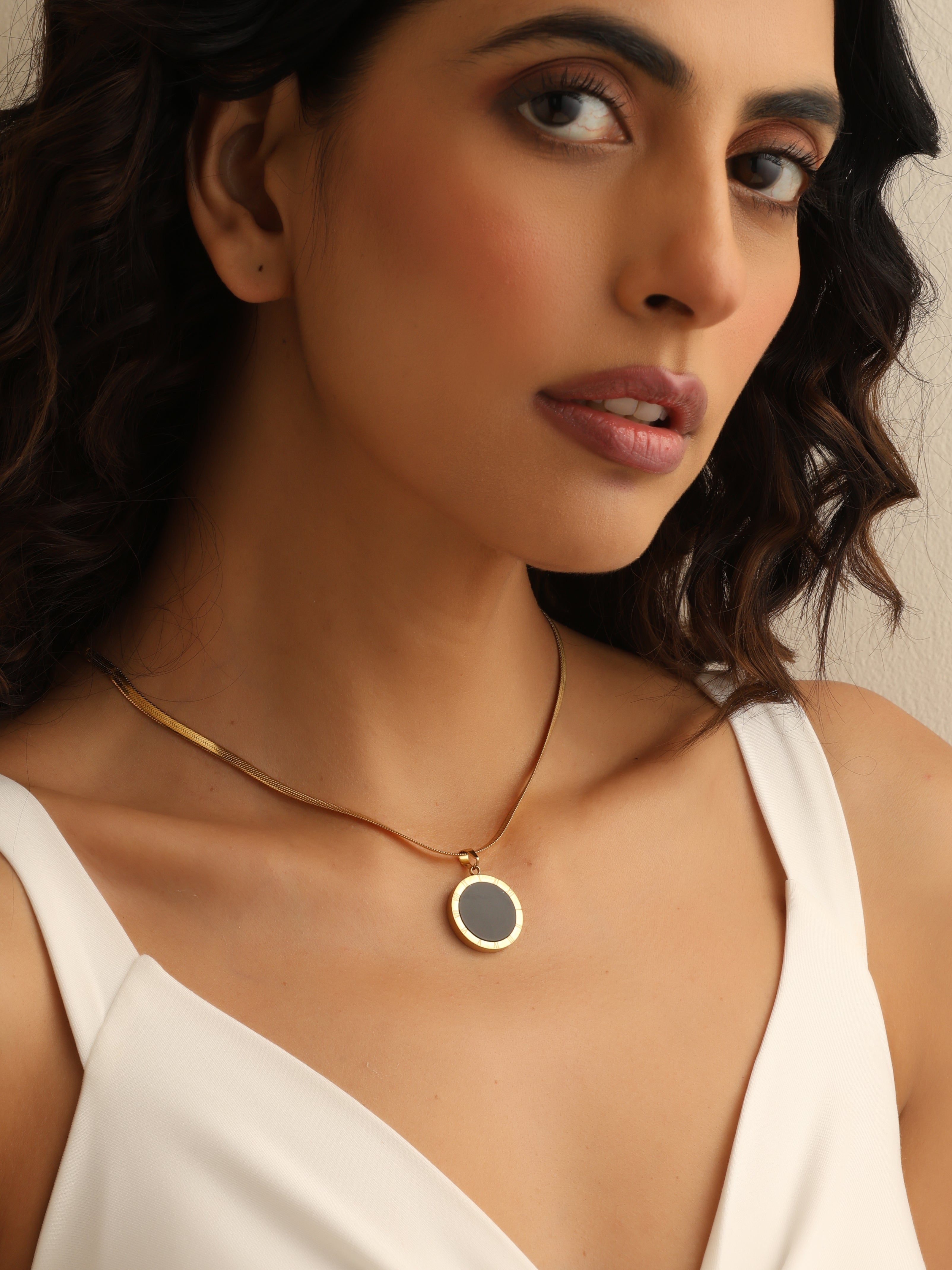 Woman wearing a gold necklace with a black pendant against a neutral background