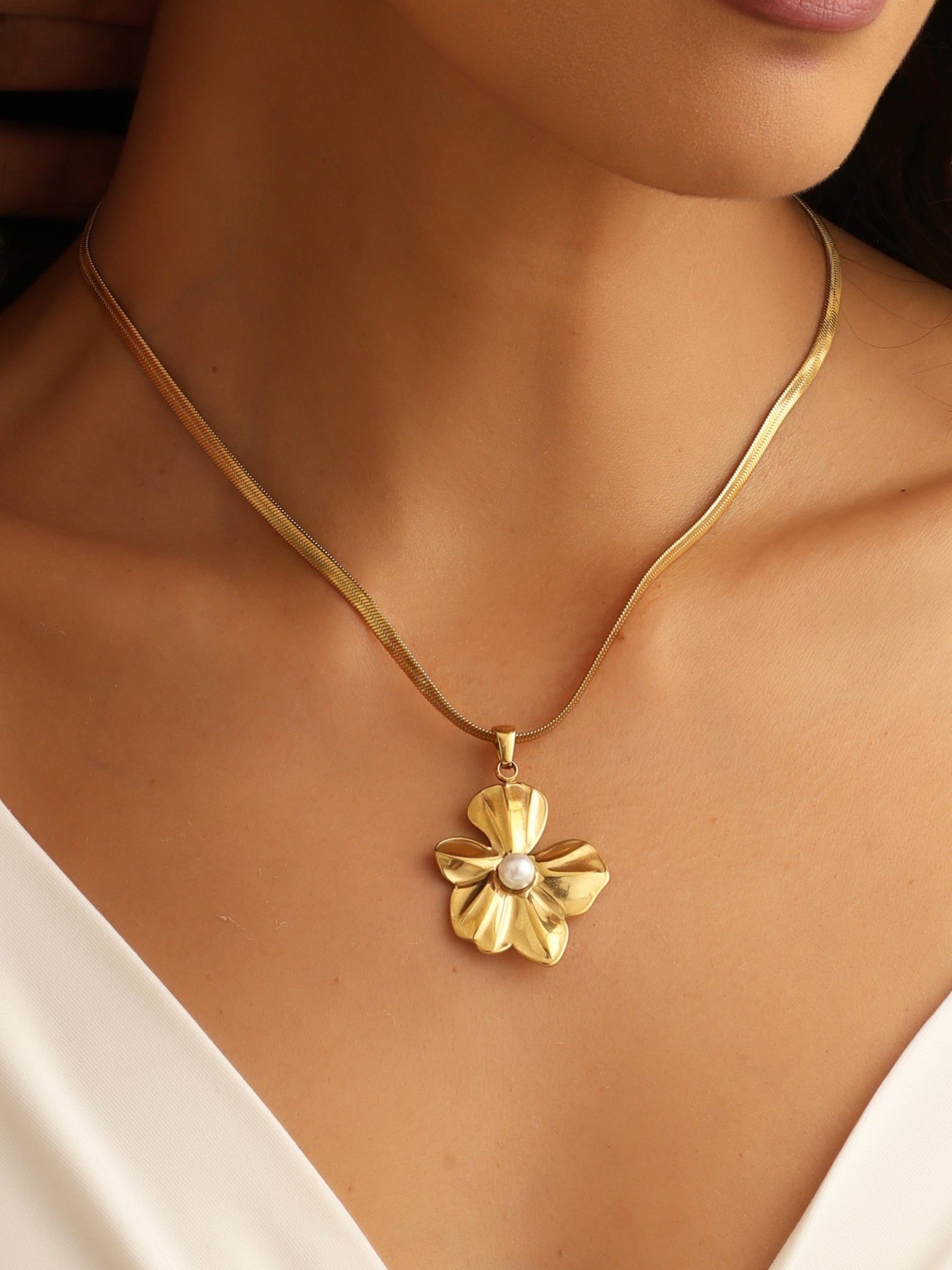 Gold necklace with a floral pendant worn by a person in a white top.
