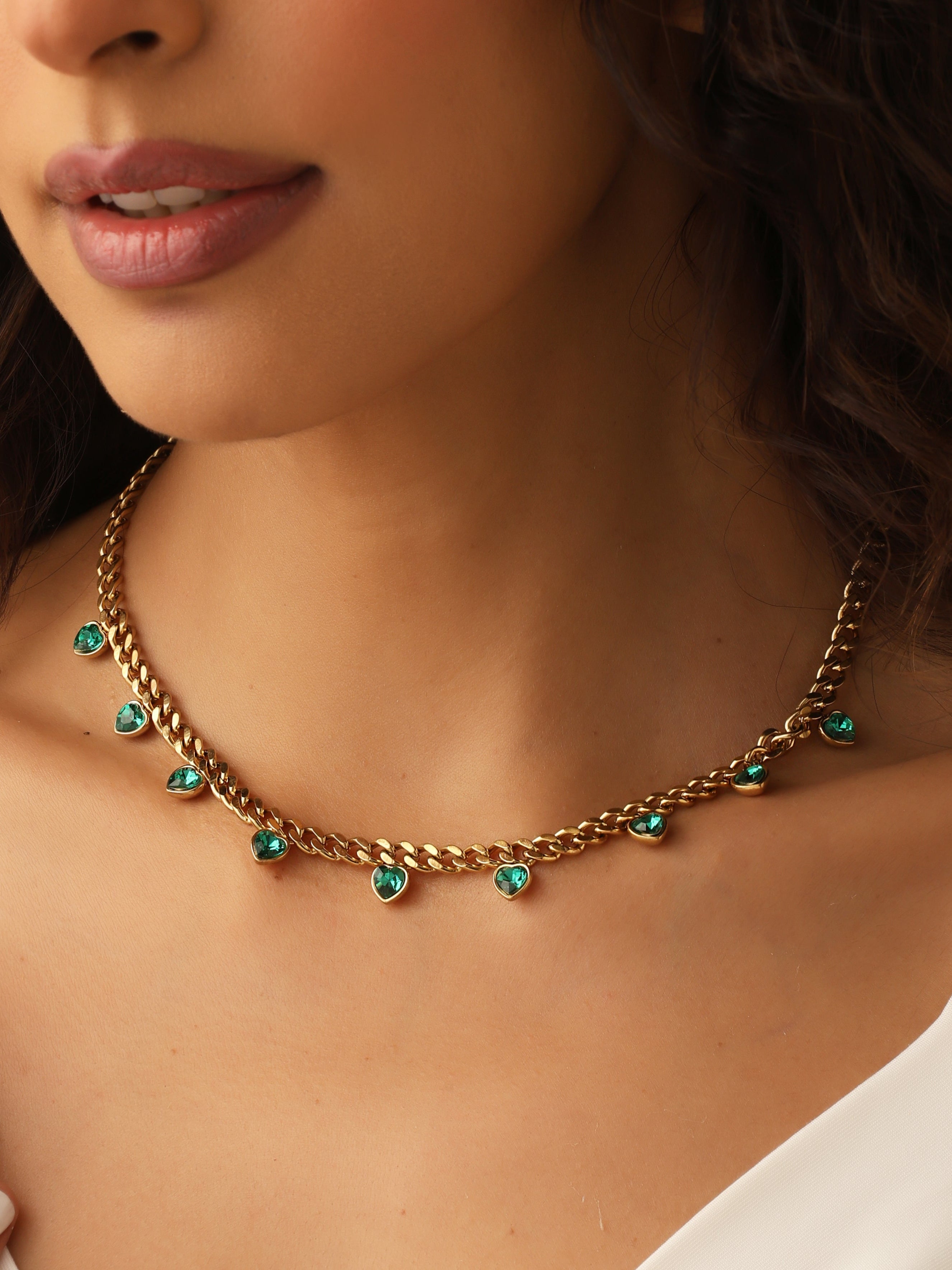 Close-up of a person wearing a gold necklace with green gemstones.