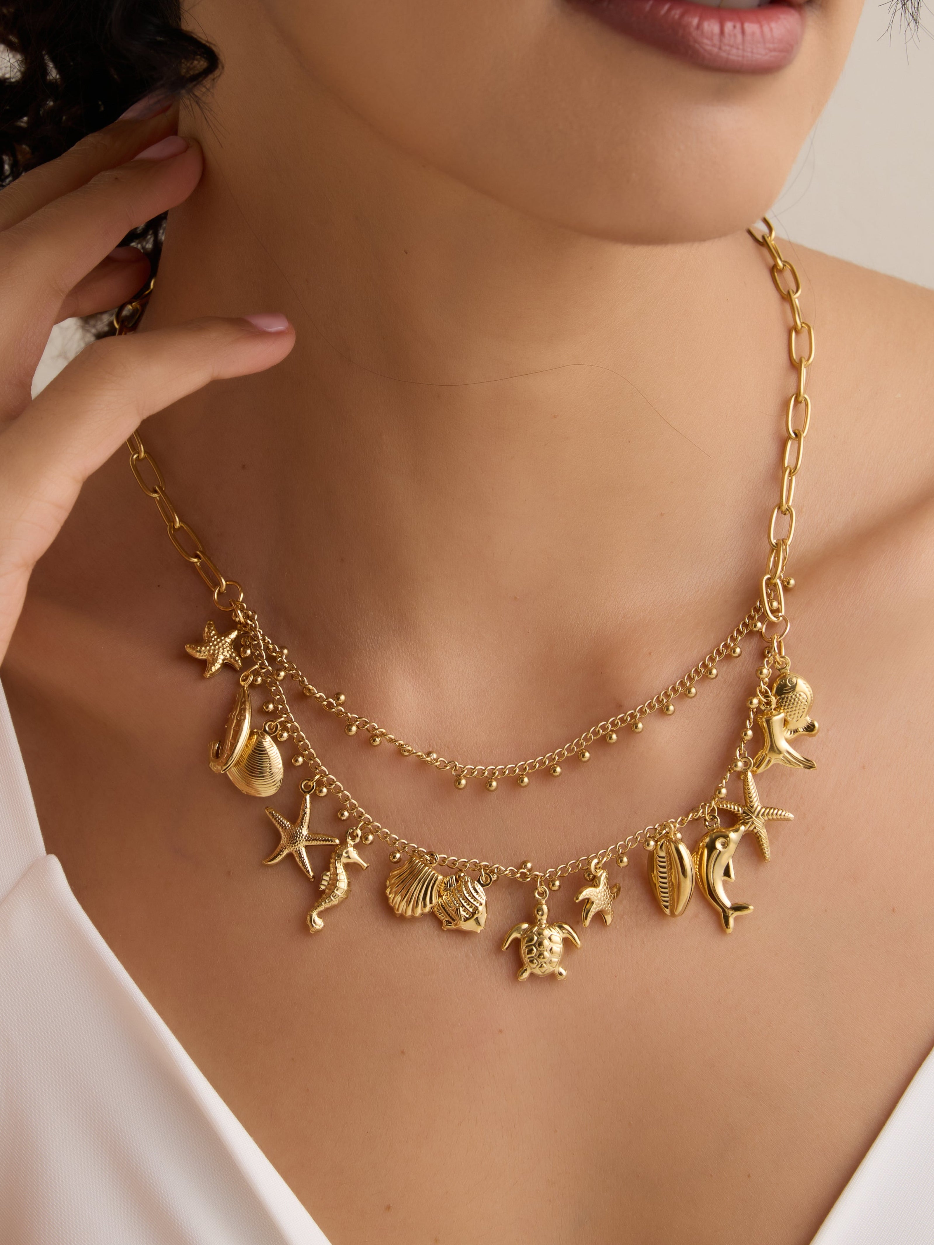 Gold necklace with charms worn by a person against a neutral background