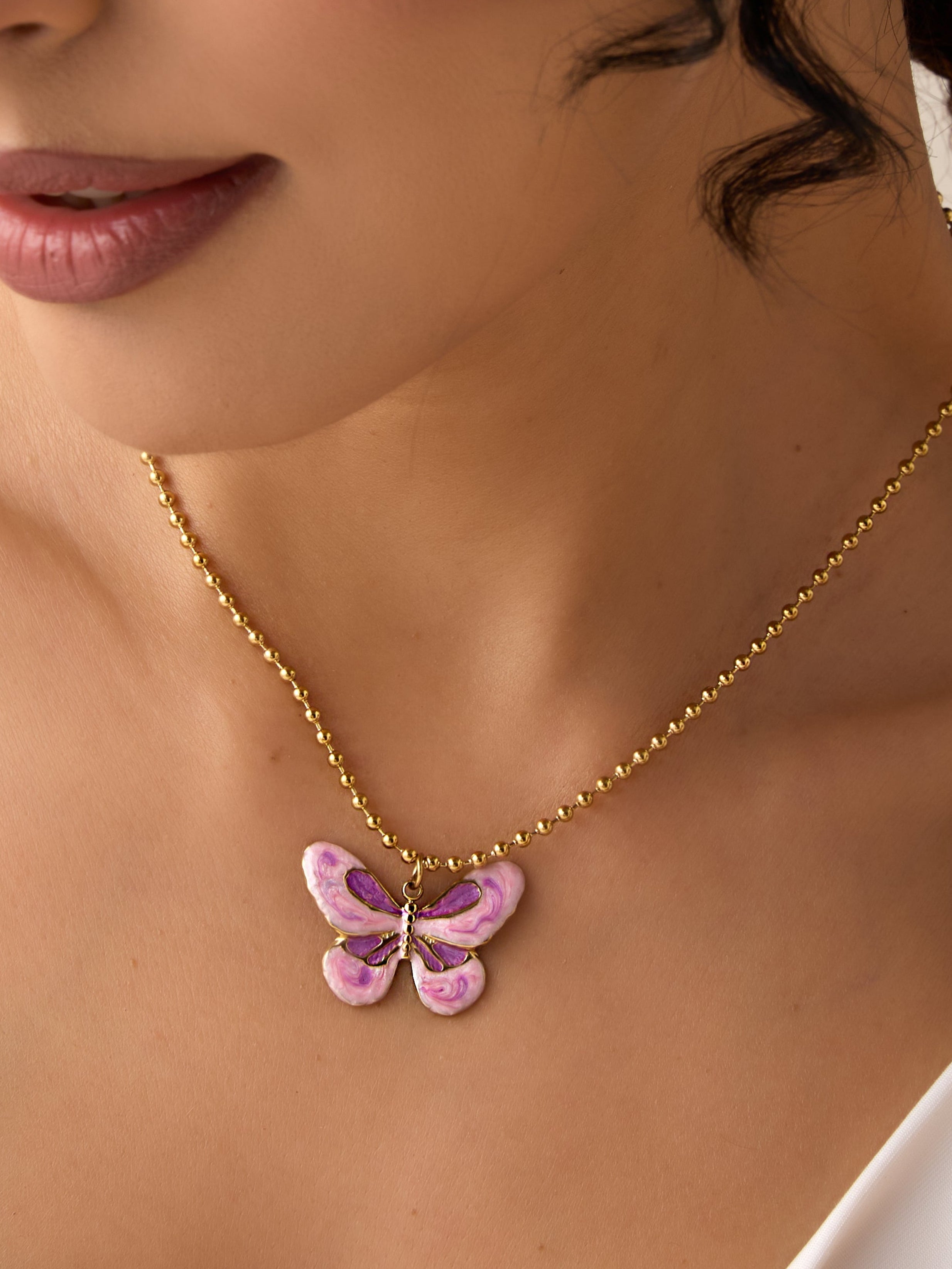 Close-up of a woman wearing a gold necklace with a butterfly pendant.
