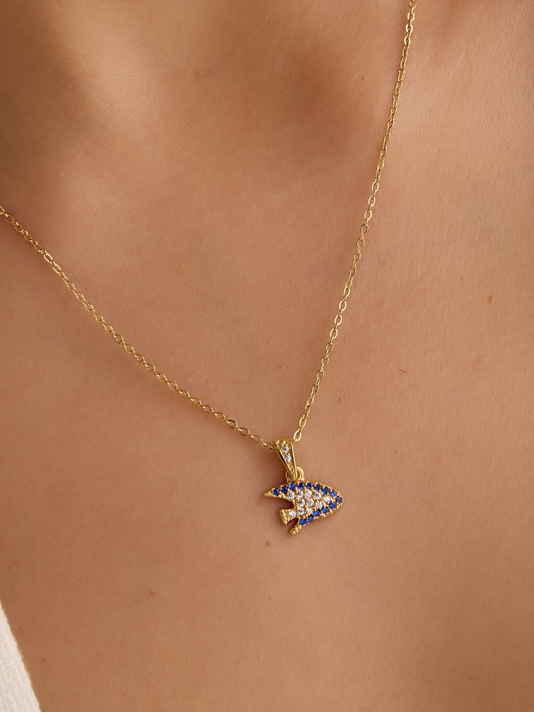 Close-up of a person wearing a gold necklace with a blue and gold pendant.