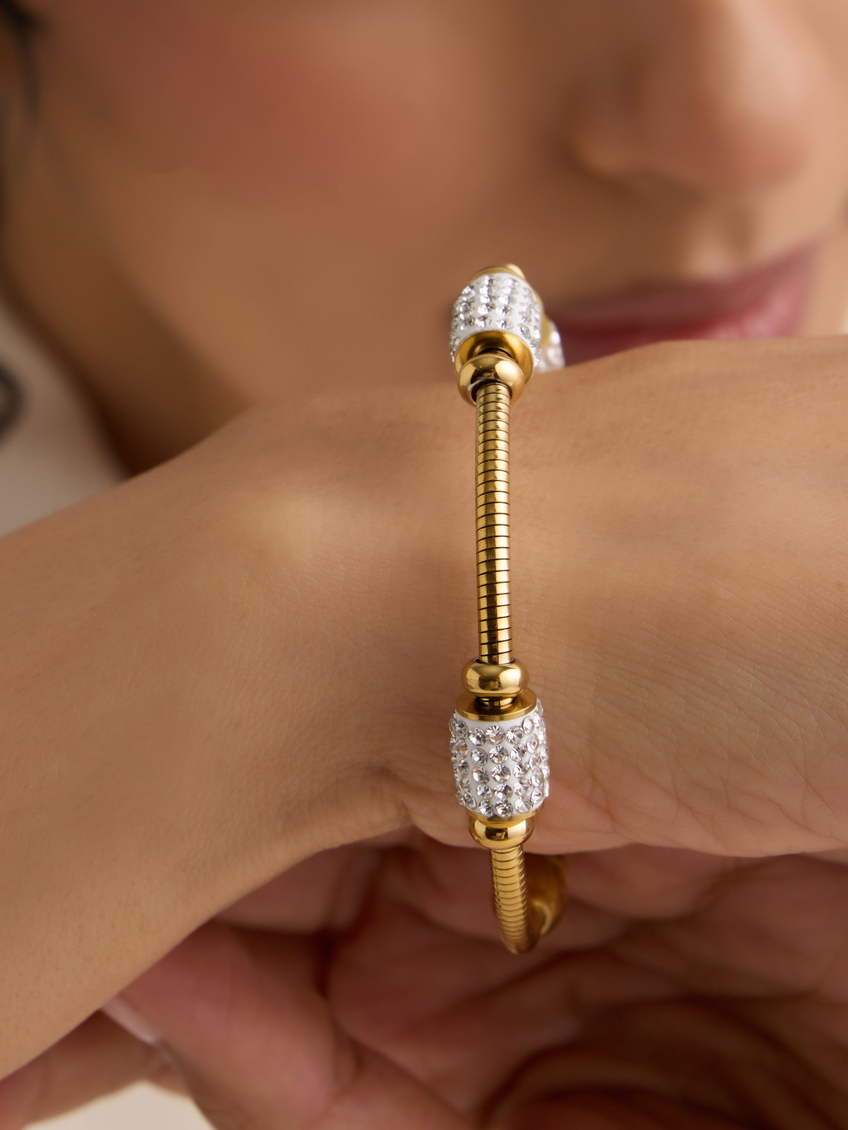 Close-up of a person wearing a gold and diamond bracelet on a neutral background