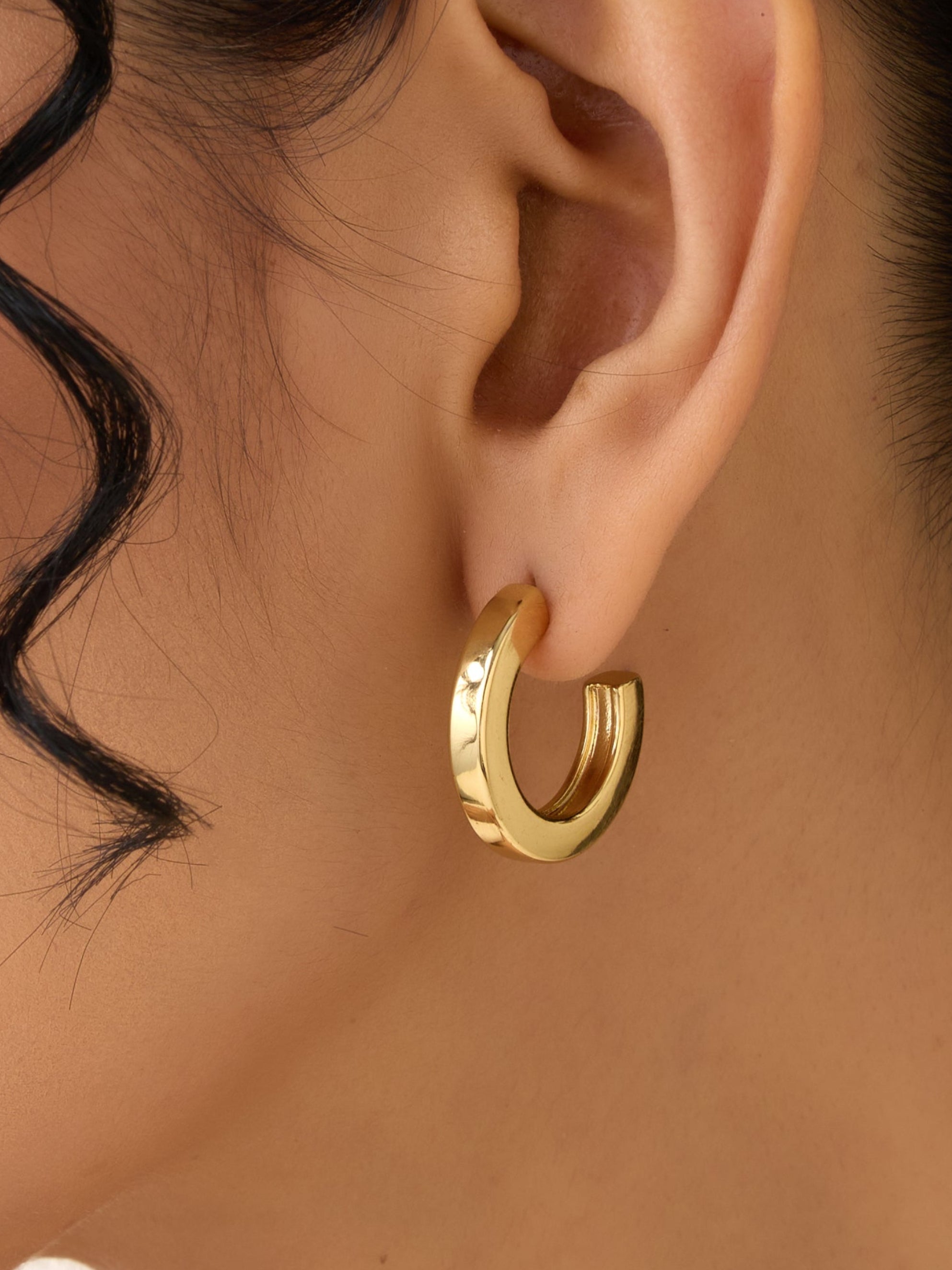 Close-up of an ear wearing a gold hoop earring with a blurred background