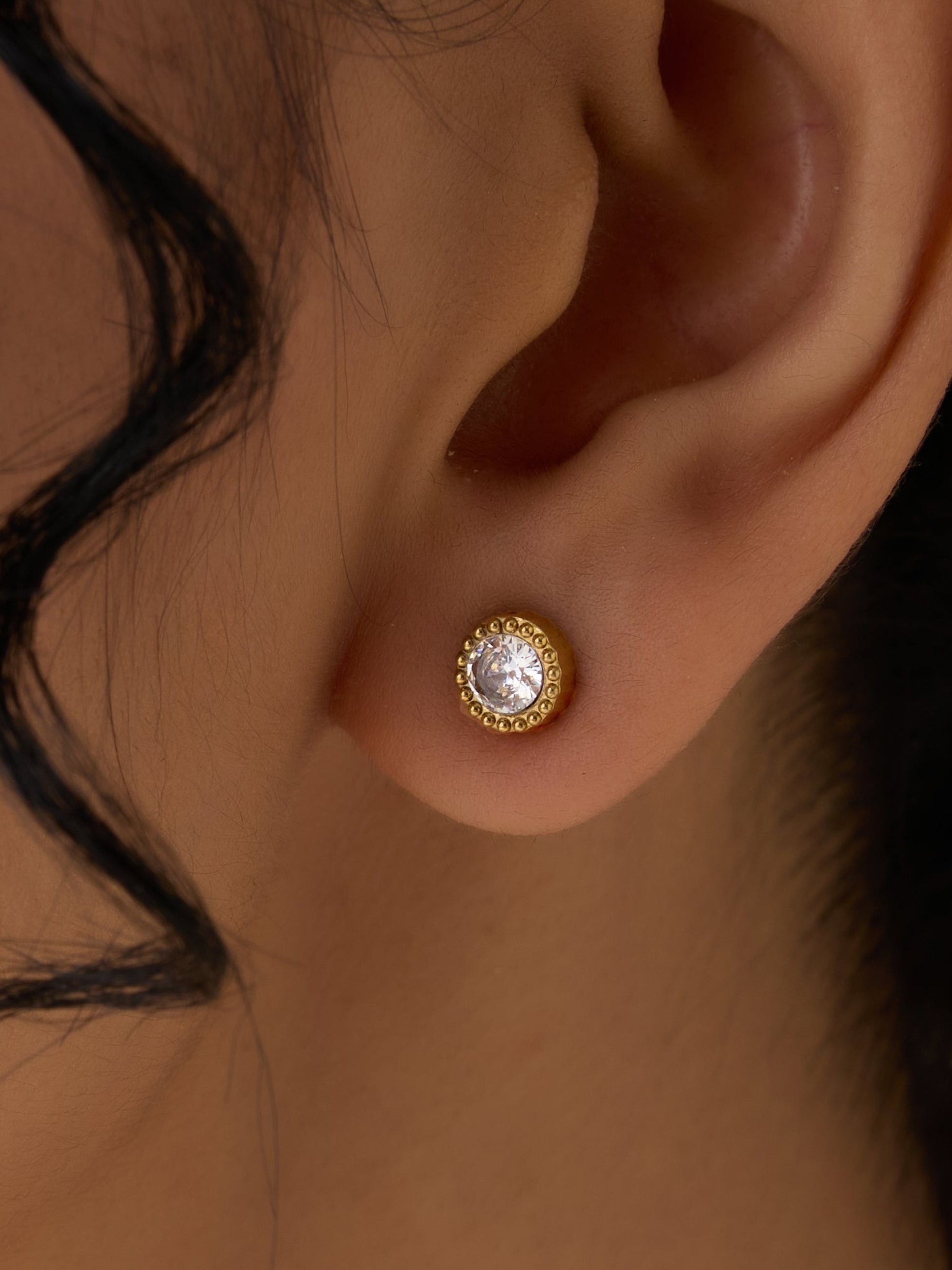 Close-up of a person wearing a gold earring with a clear gemstone.