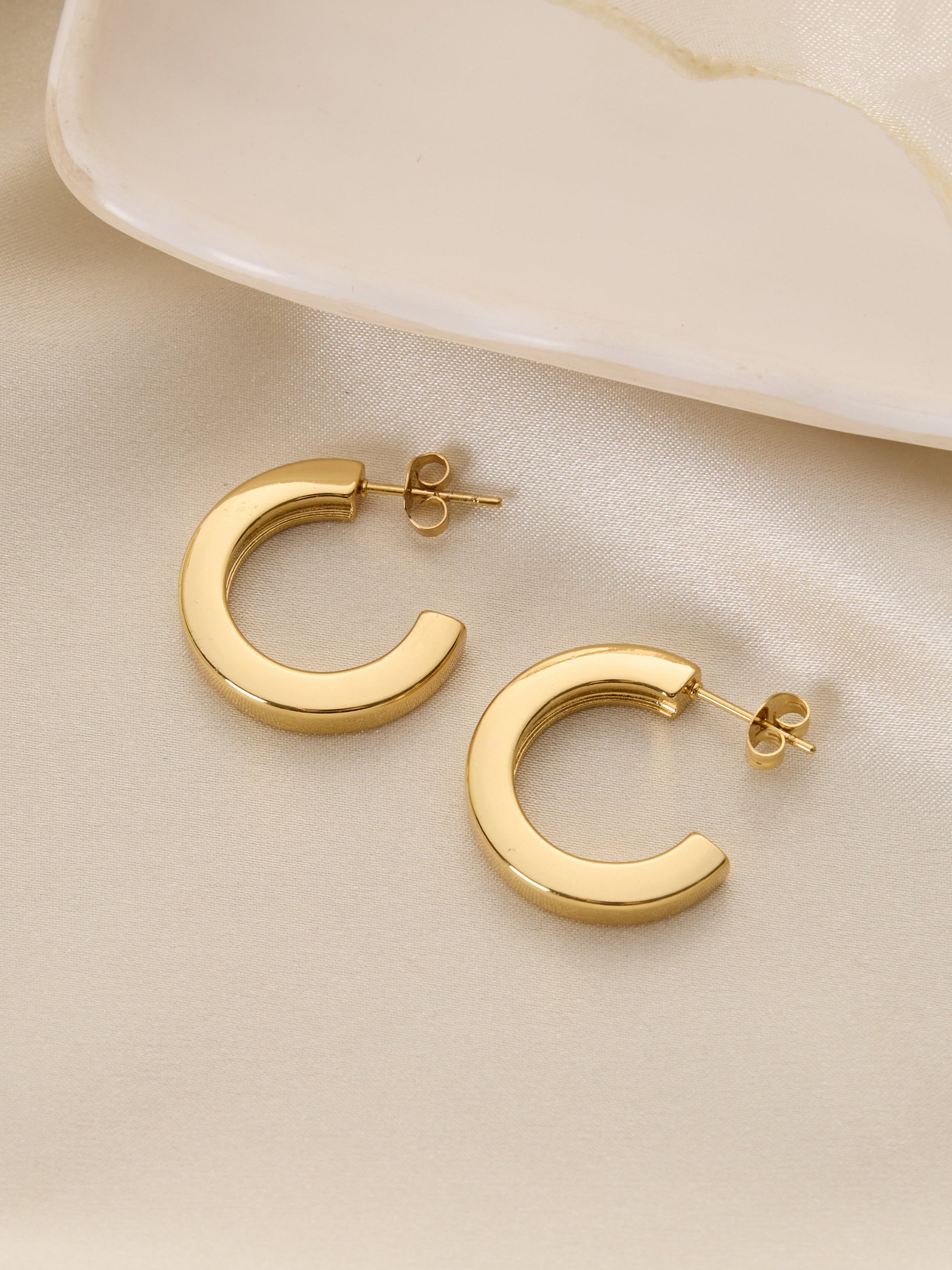 Gold hoop earrings on a soft beige fabric background
