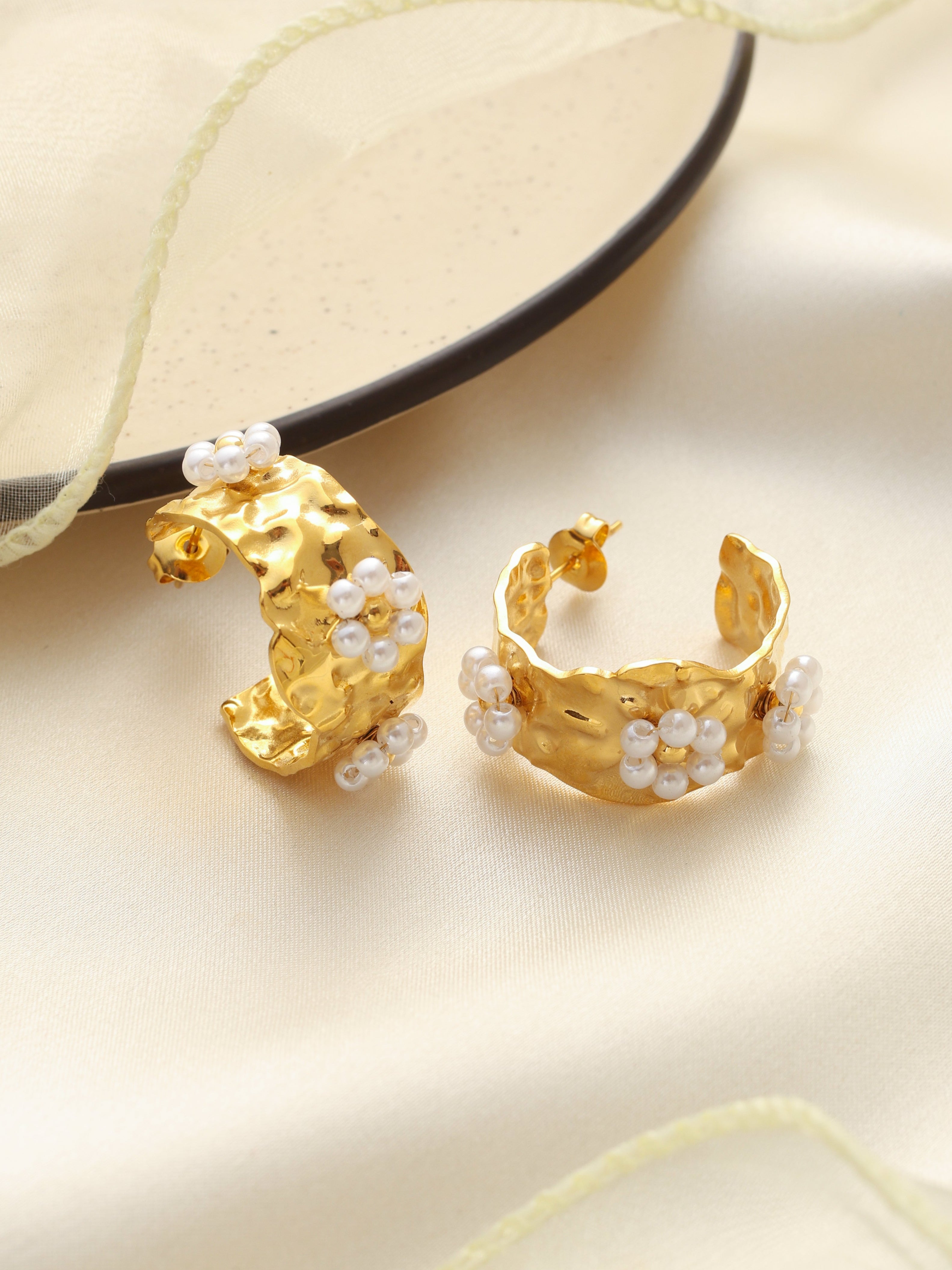 Gold hoop earrings with pearl accents on a beige fabric background