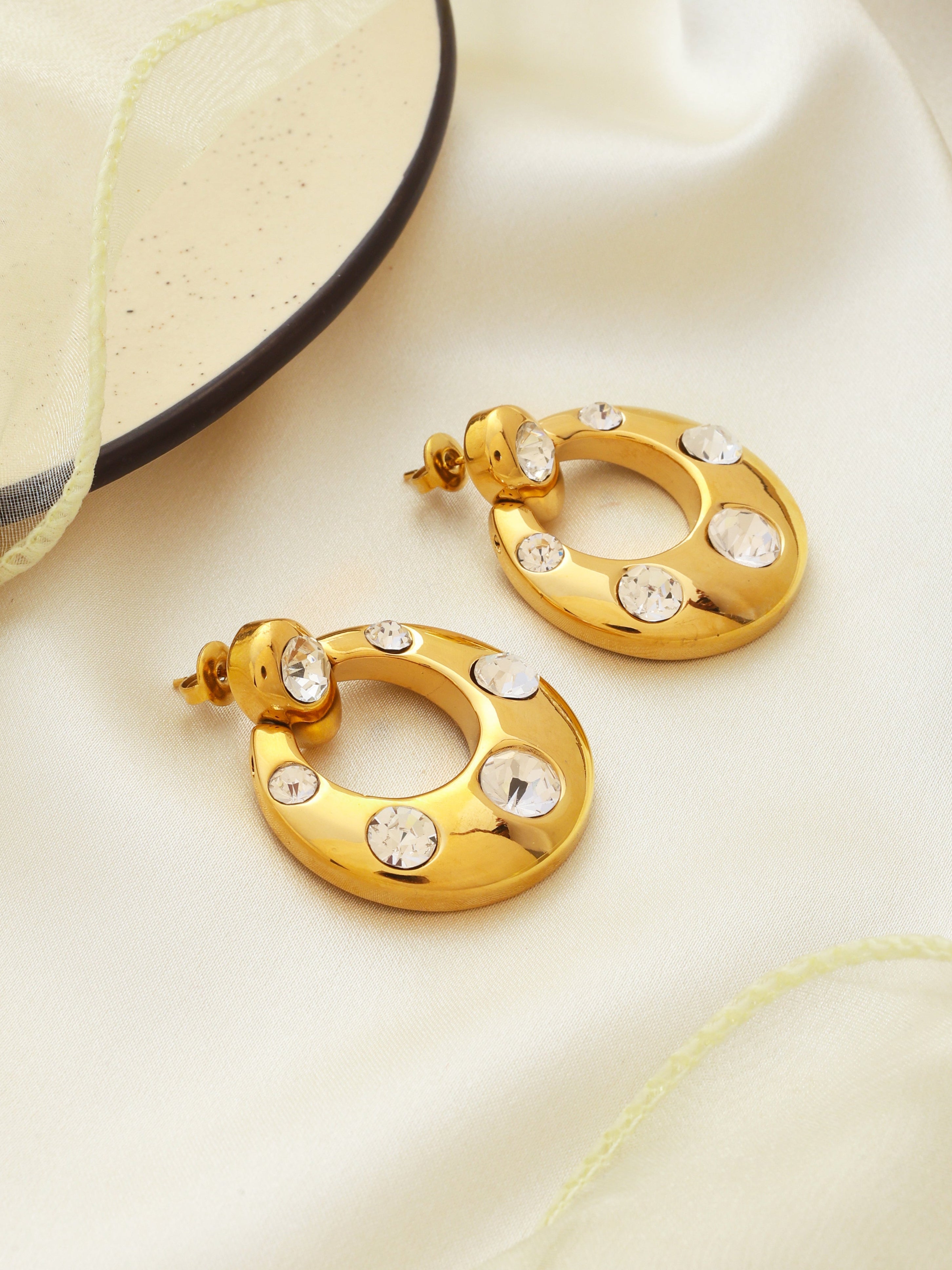 Gold hoop earrings with embedded stones on a light fabric background