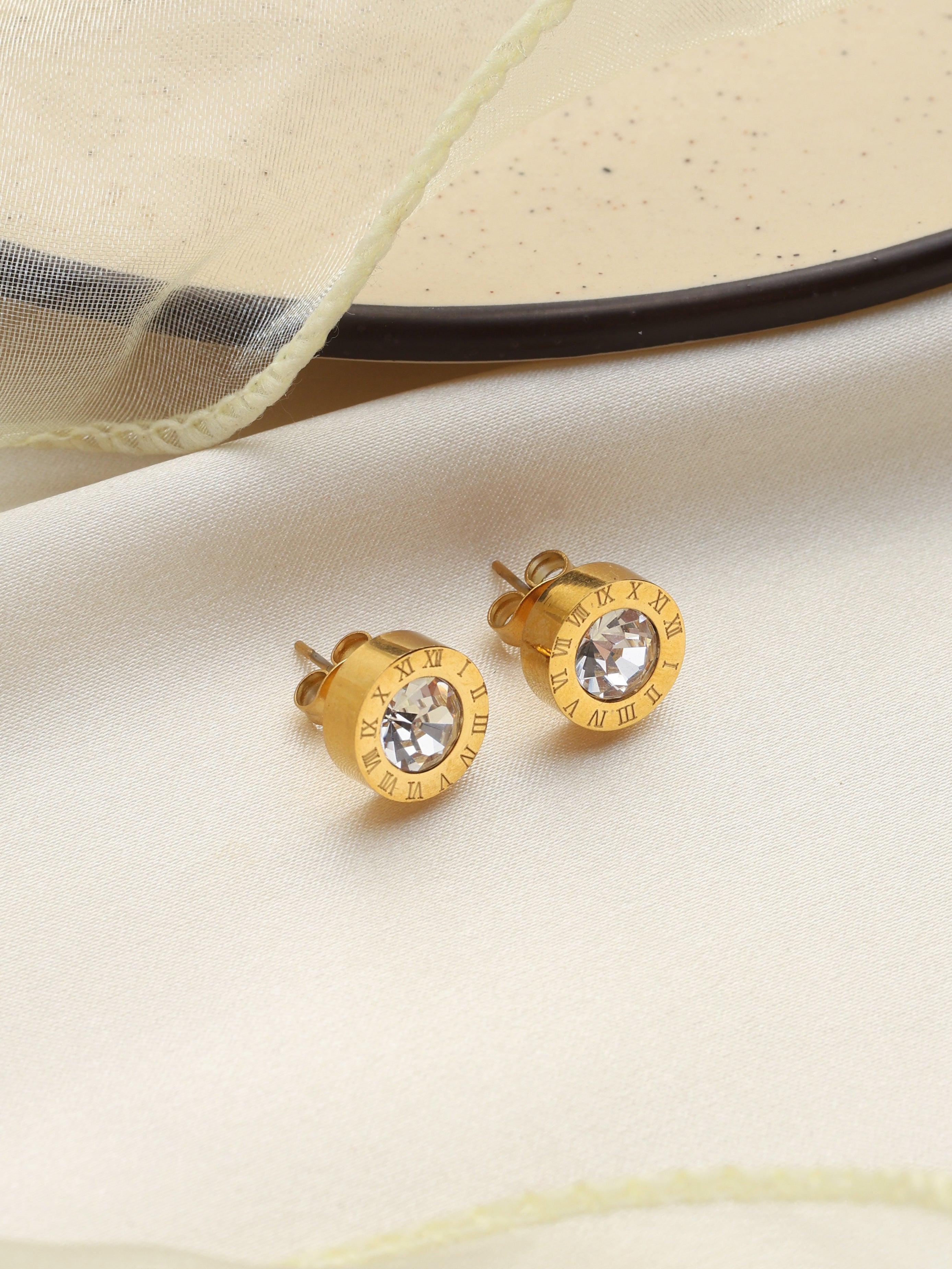 Gold stud earrings with clear gemstones on a beige fabric background