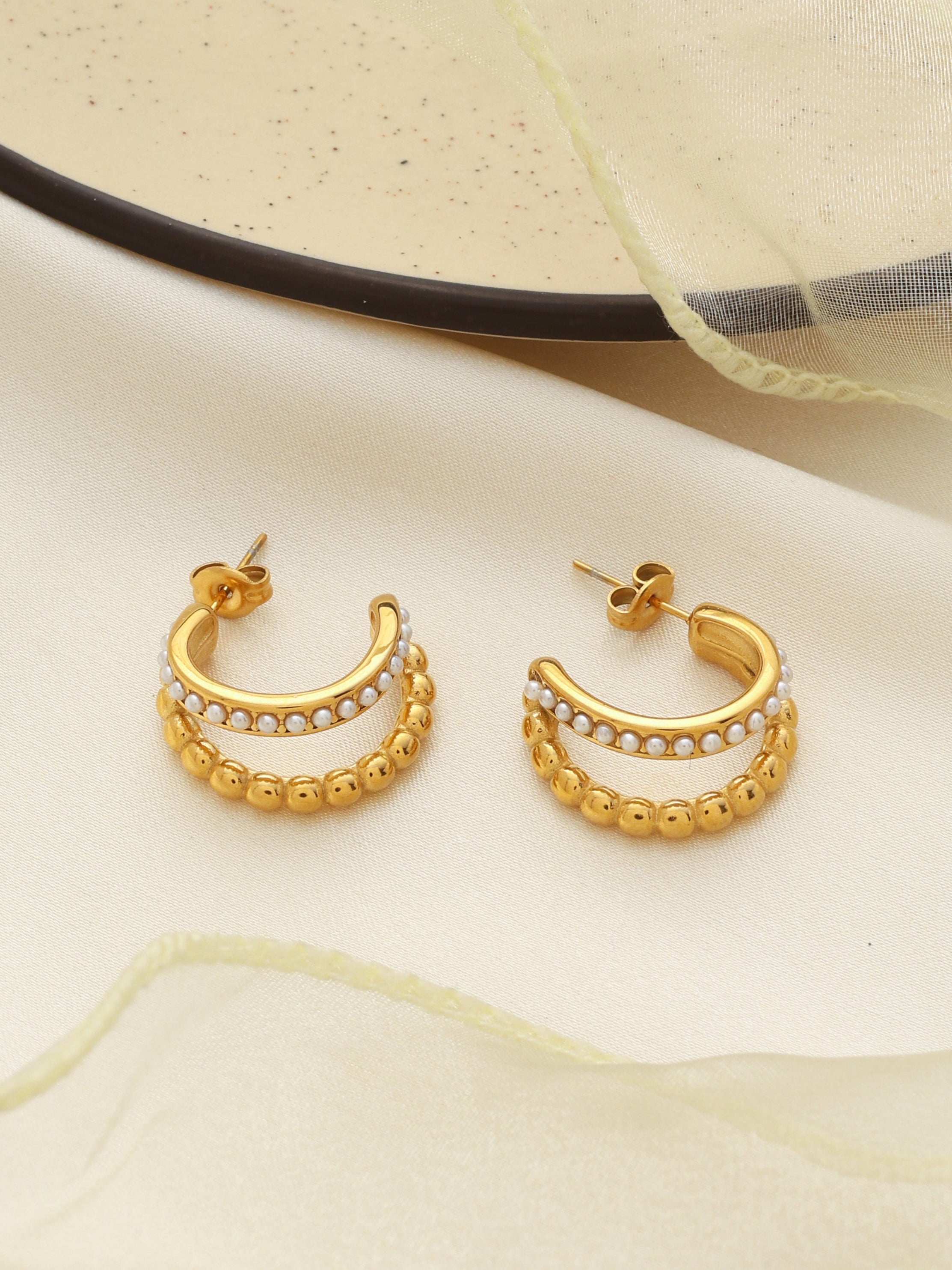 Gold hoop earrings with pearl accents on a light fabric background