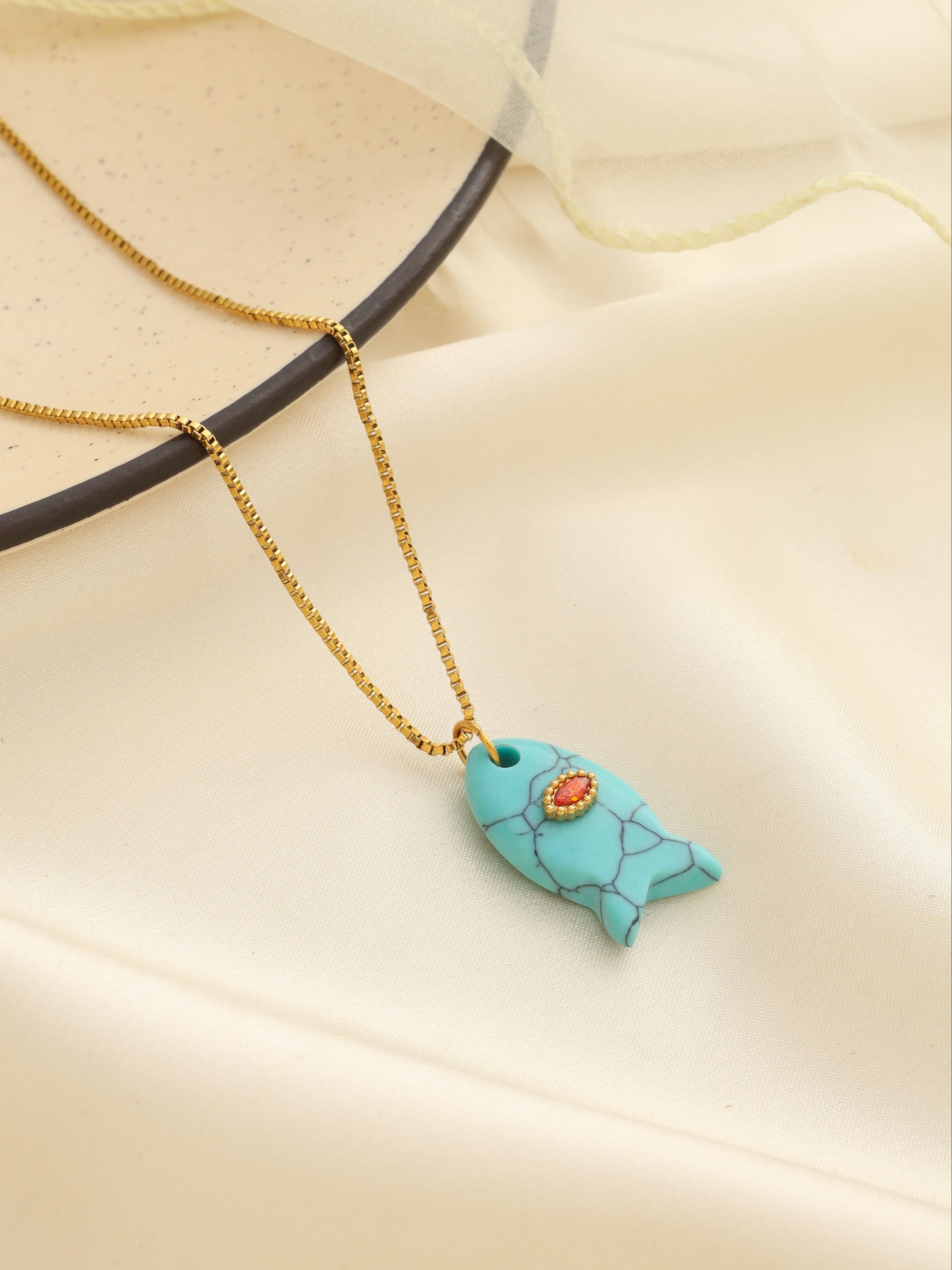 Necklace with a turquoise fish pendant on a beige background