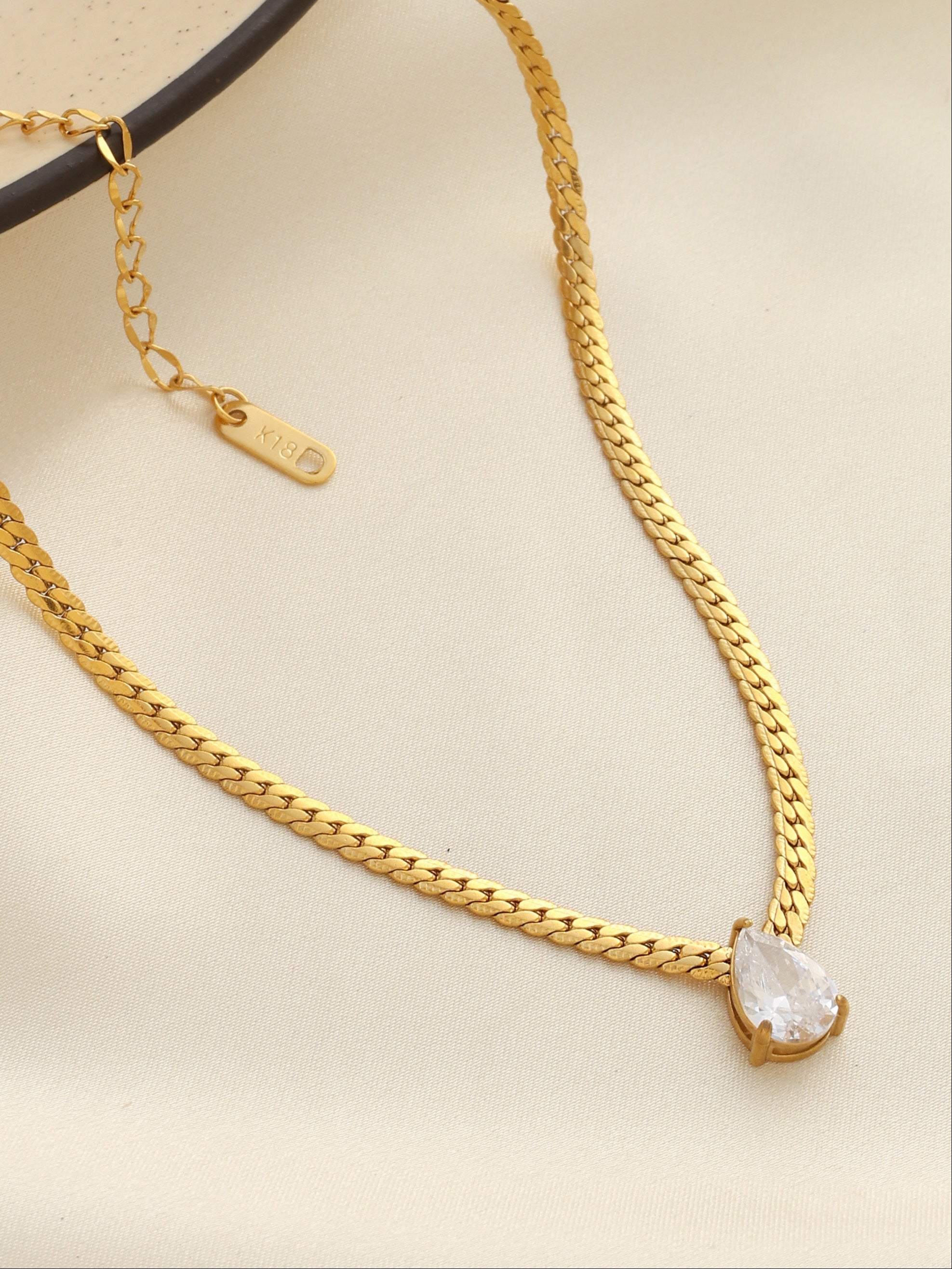 Gold chain necklace with a heart-shaped pendant on a beige background