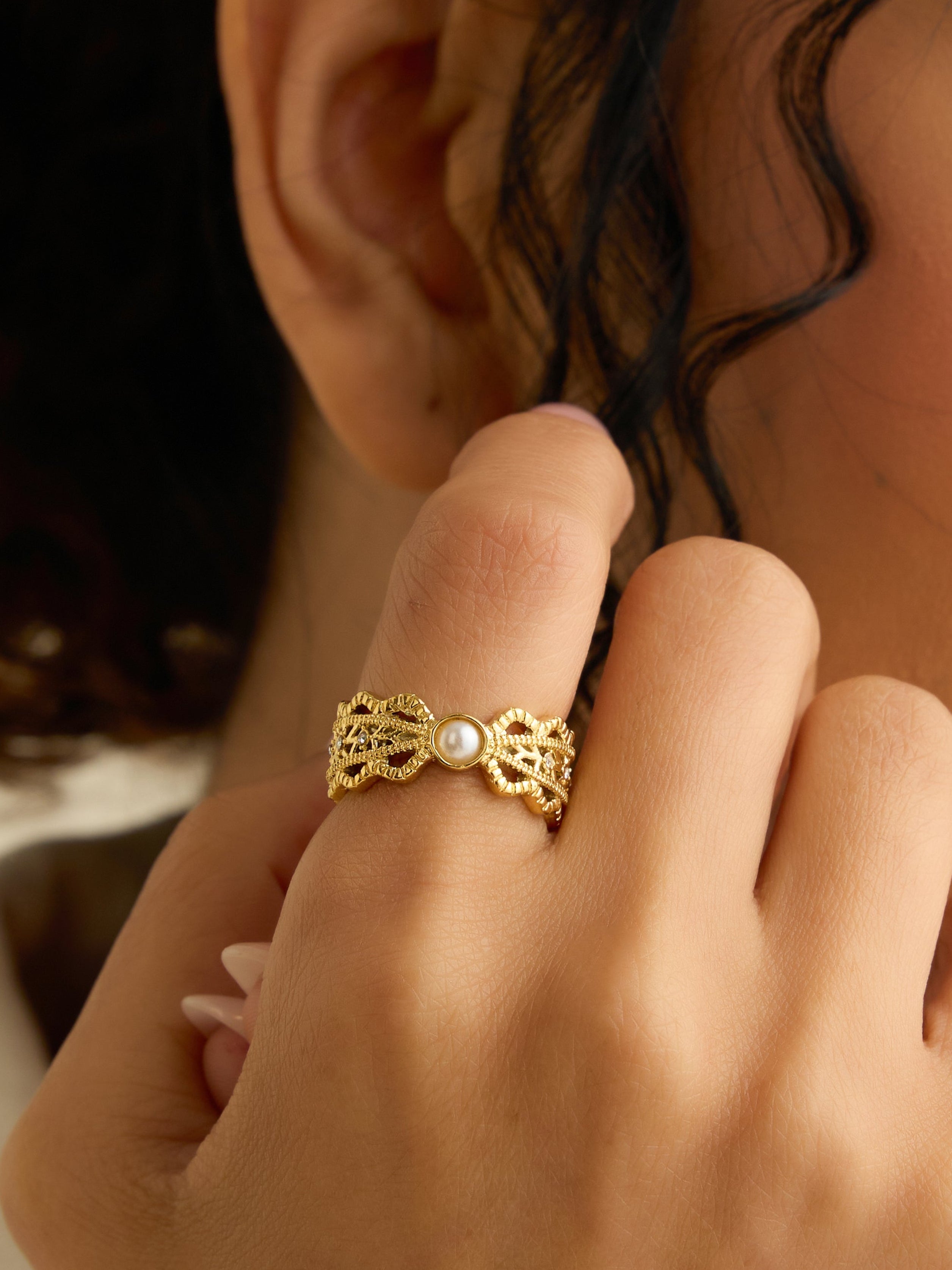 Woman wearing a gold ring with a pearl on her finger, adjusting an earring.