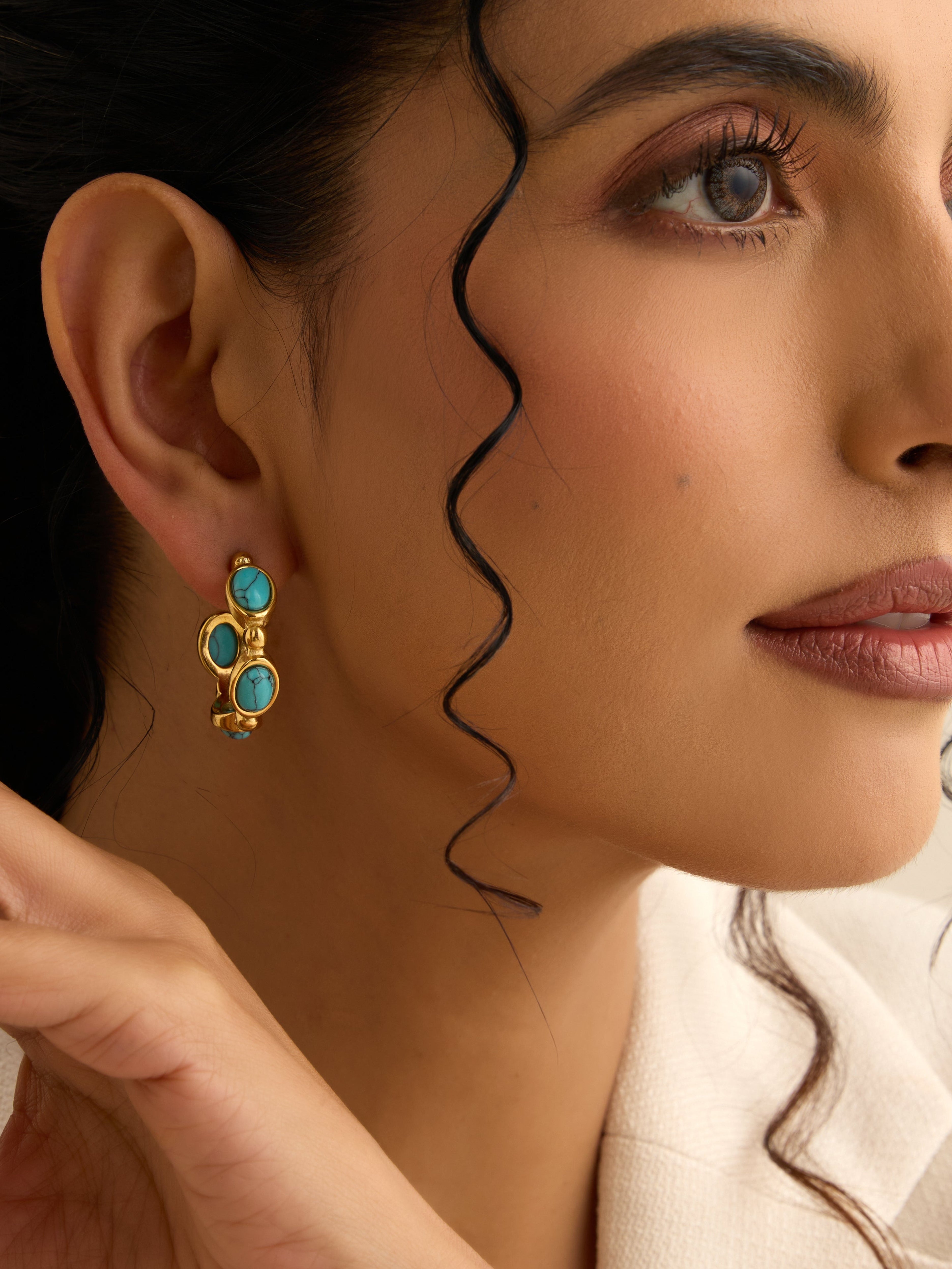 Close-up of a woman wearing gold earrings with turquoise stones, focusing on the jewelry.