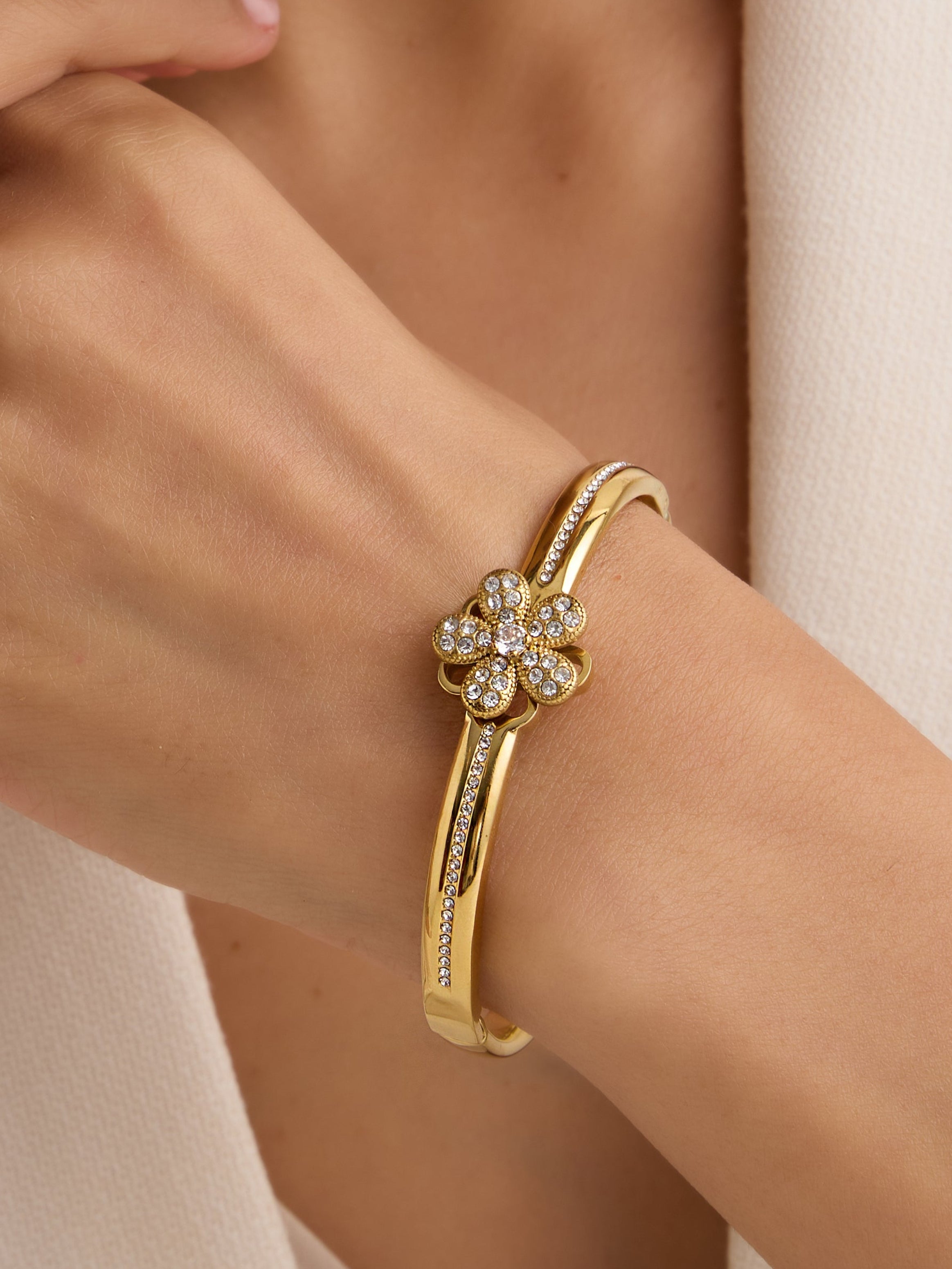 Gold bracelet with diamond accents on a person's wrist, wearing a light-colored outfit.