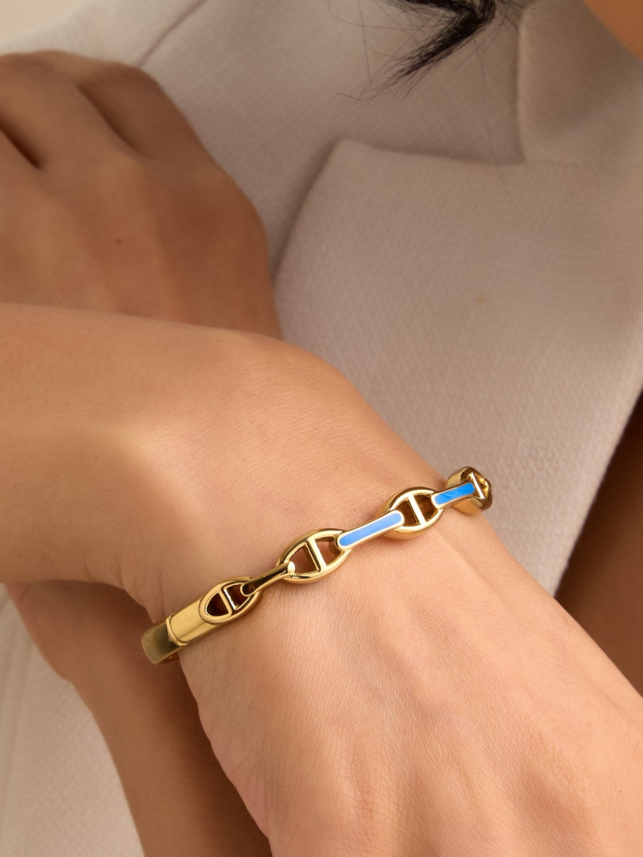 Close-up of a hand wearing a gold bracelet with a neutral background