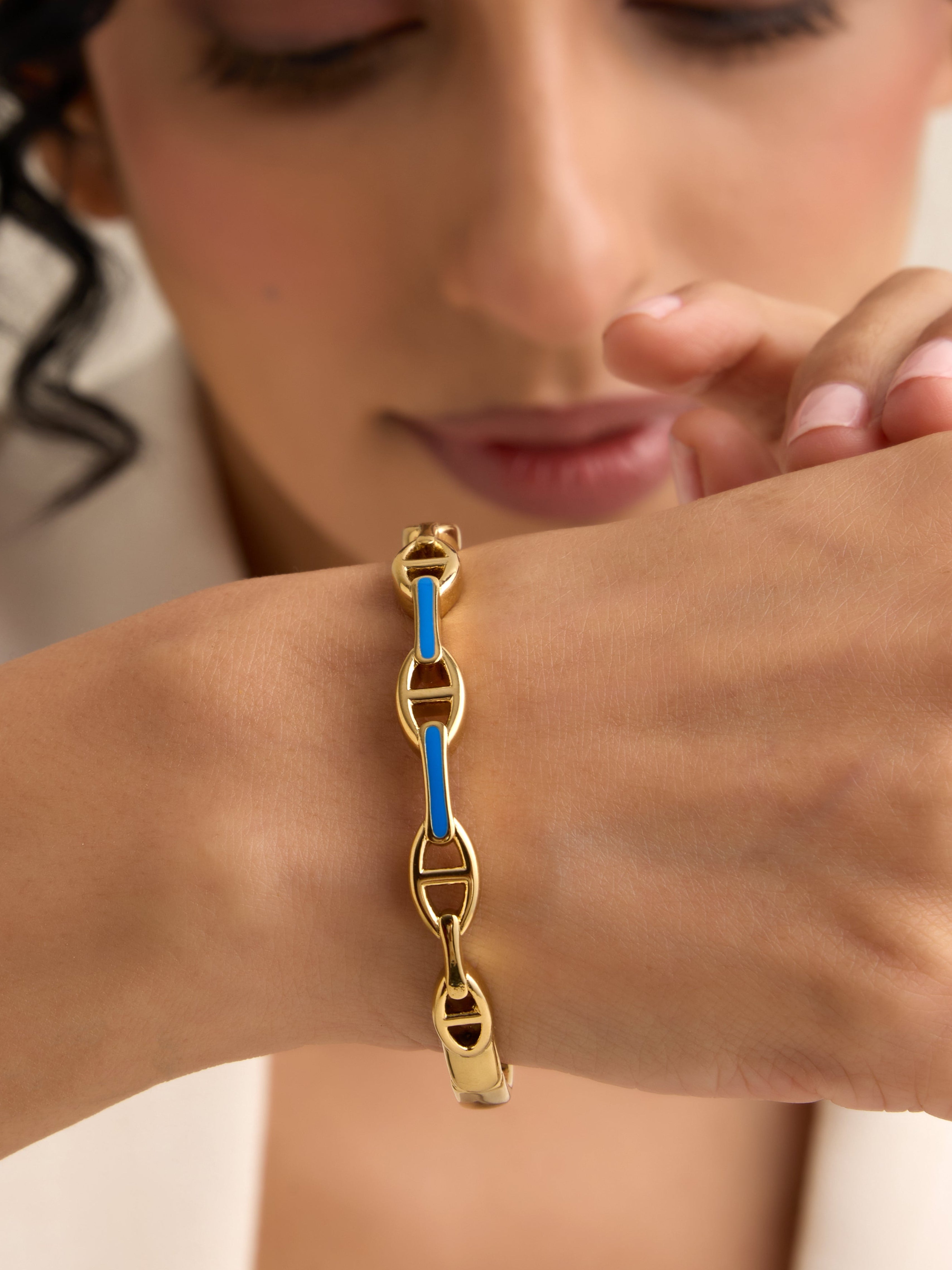 Woman wearing a gold bracelet with a blue accent on a neutral background
