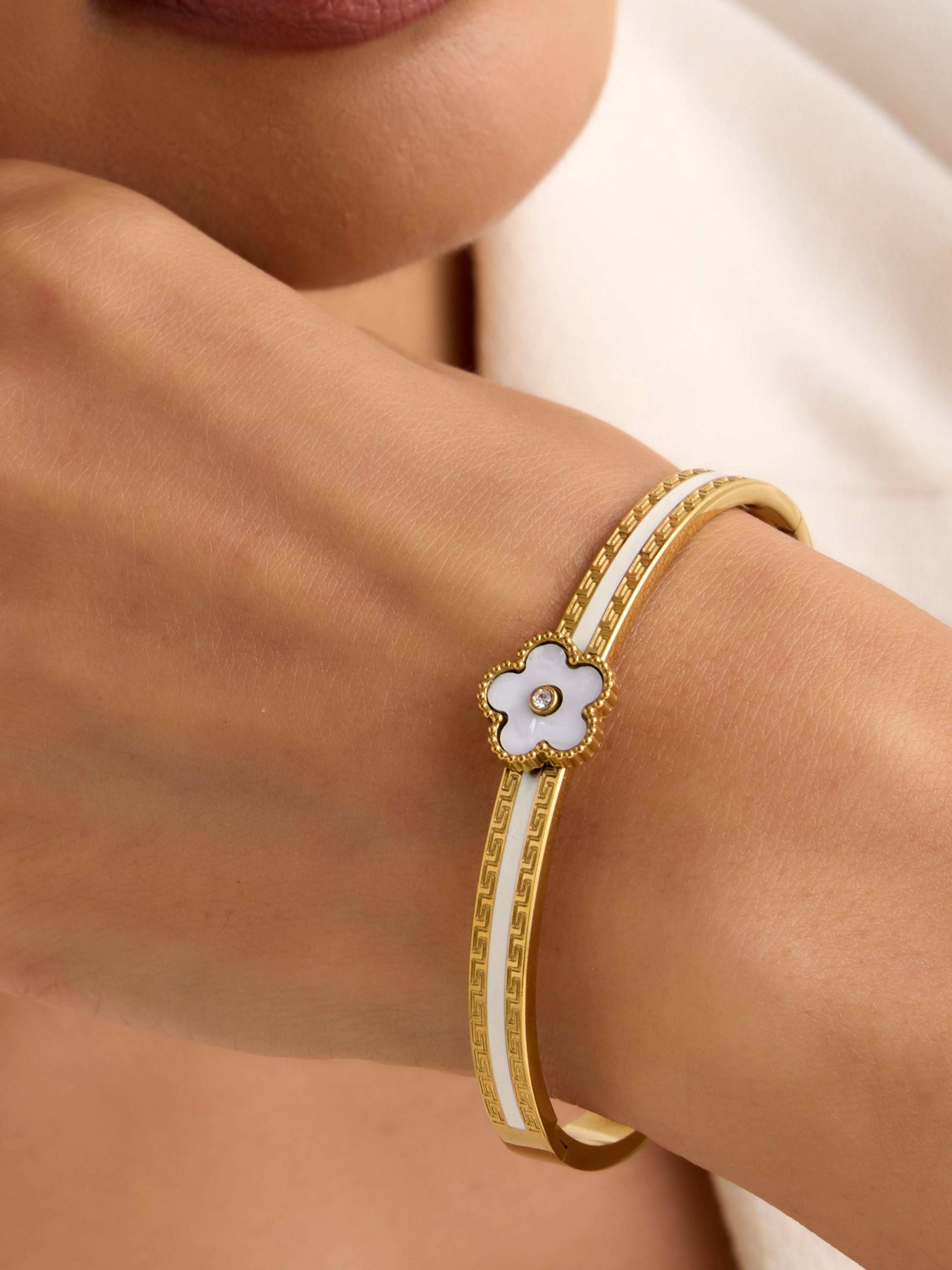 Close-up of a woman's wrist wearing a gold bracelet with a floral design against a neutral background.