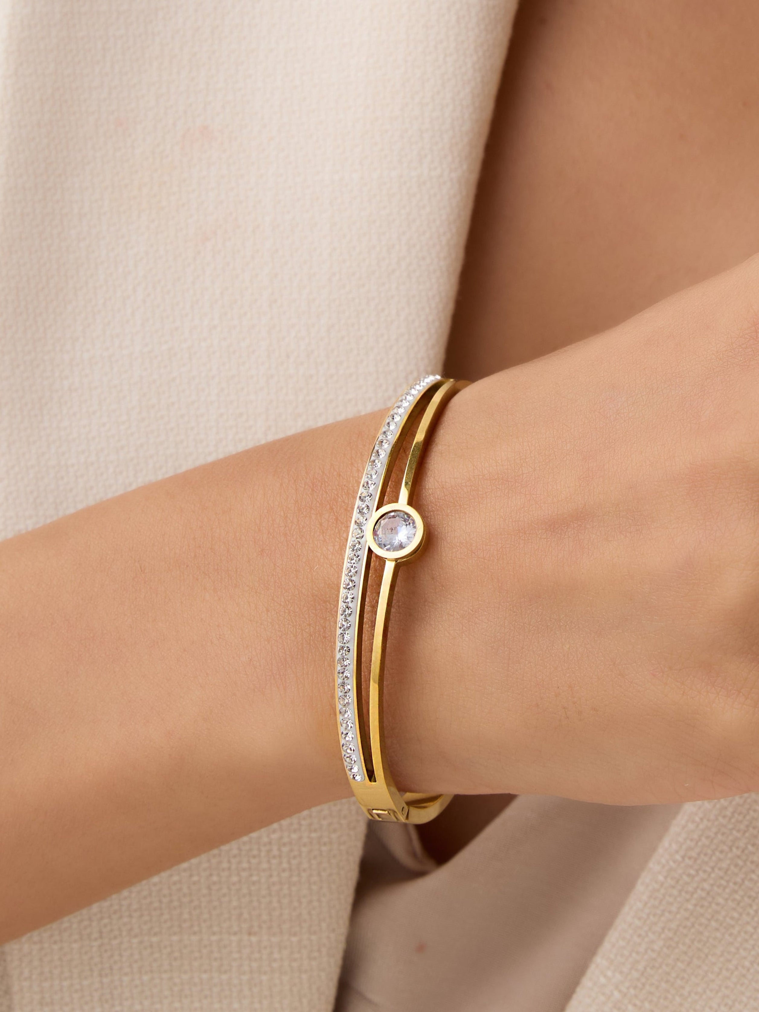 Close-up of a person wearing a gold bracelet with a diamond on a neutral background