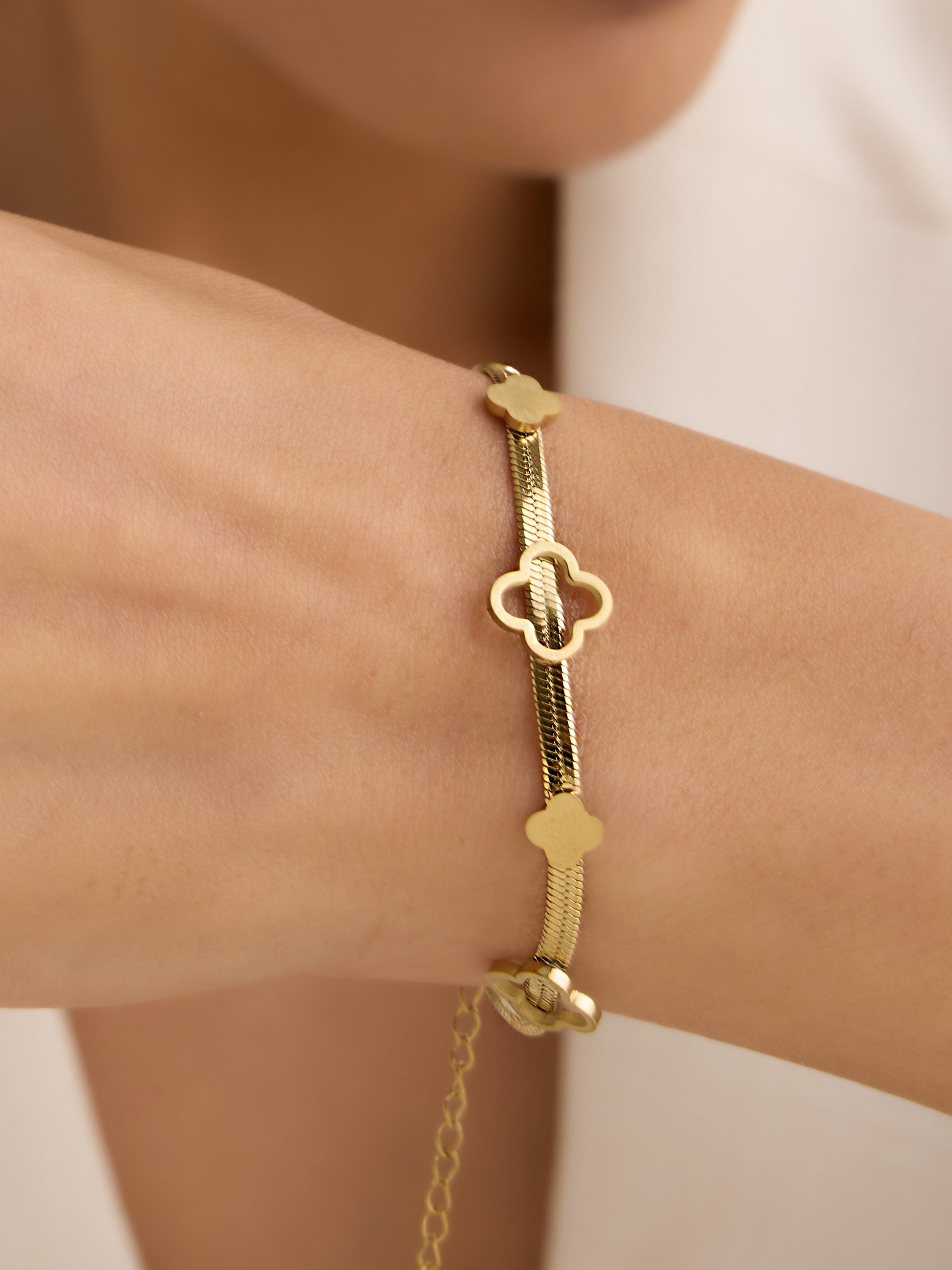 Gold bracelet with a clover design on a person's wrist against a white background
