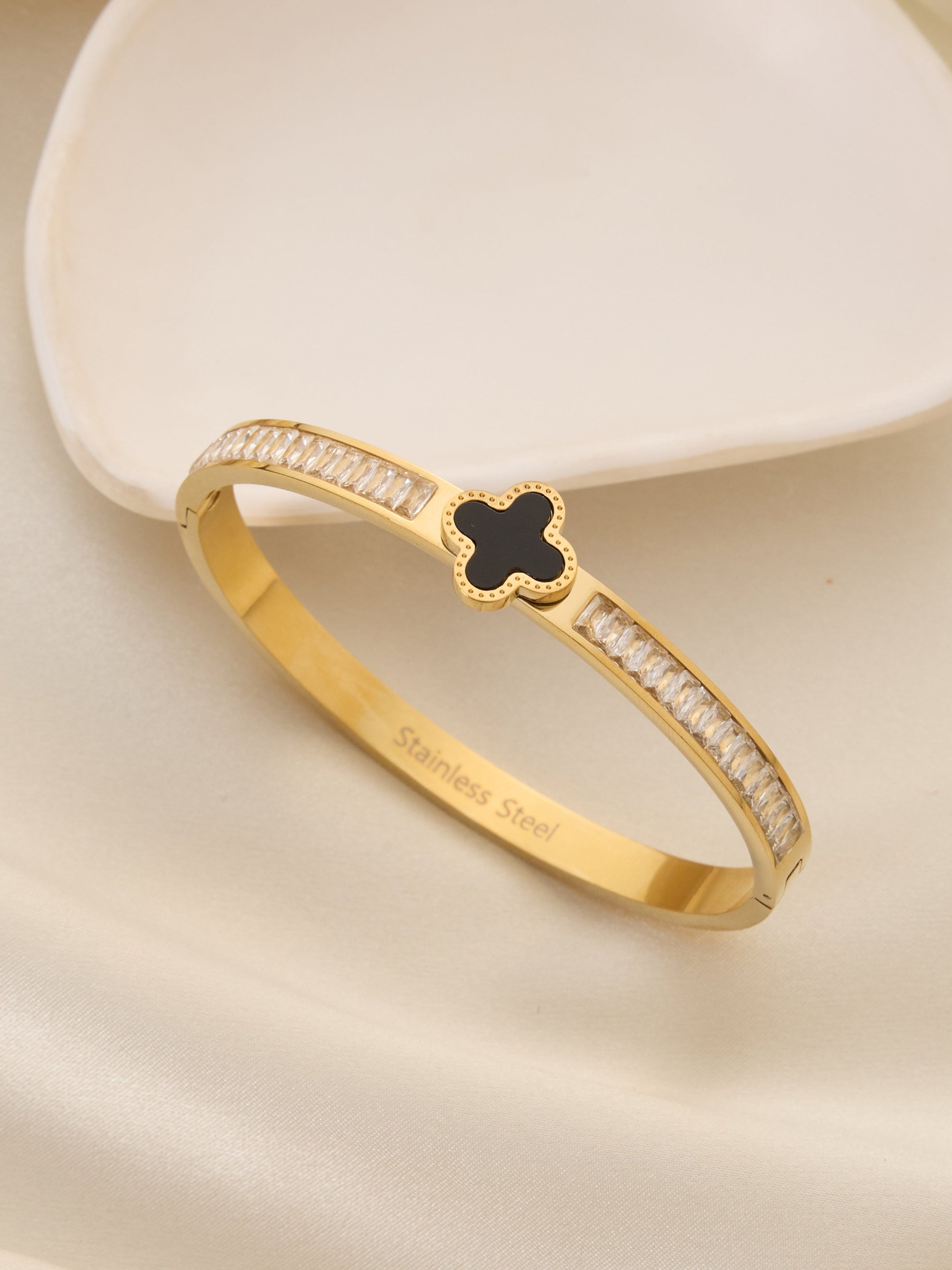 Gold bracelet with a black clover design on a beige fabric background