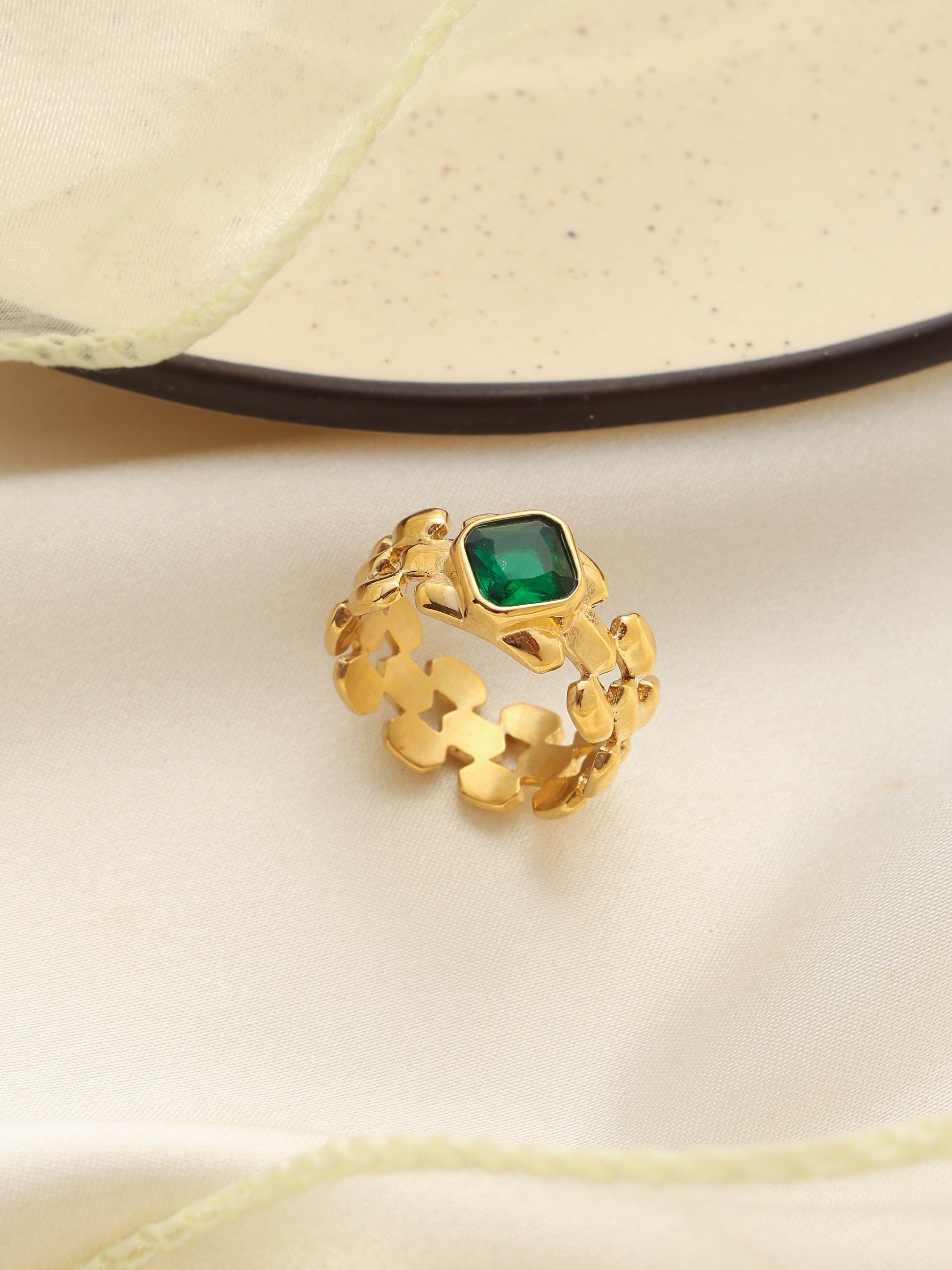 Gold ring with a green gemstone on a beige fabric background