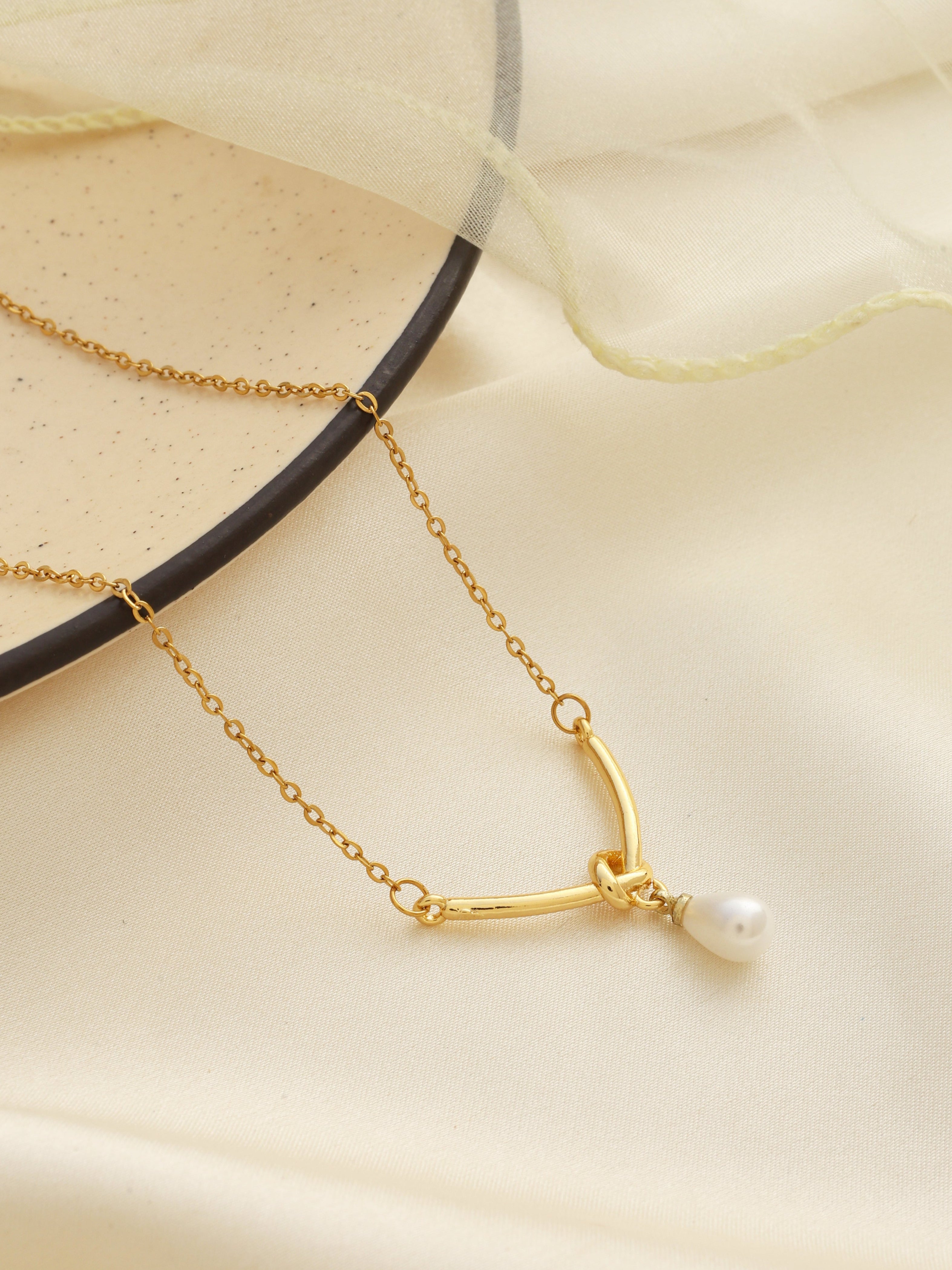 Gold necklace with a pearl pendant on a beige fabric background
