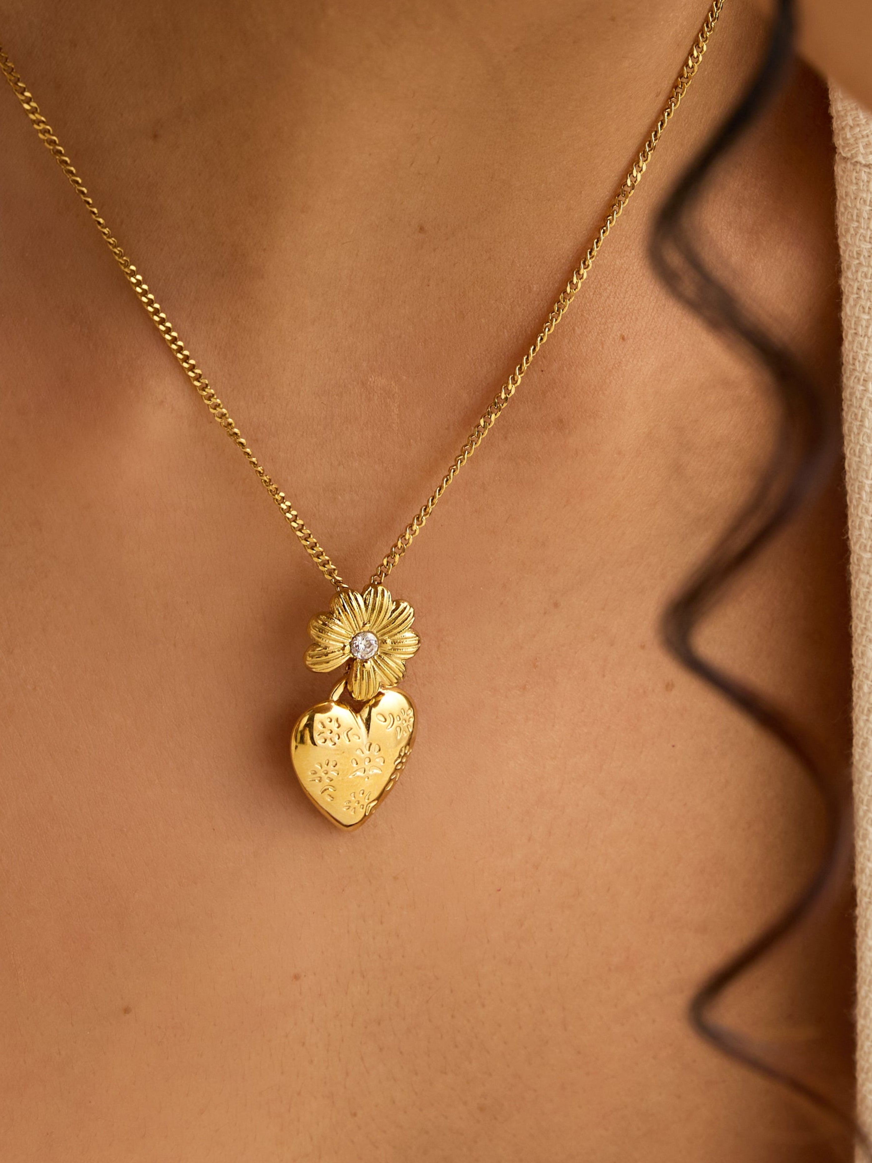 Gold necklace with a heart-shaped pendant worn by a person