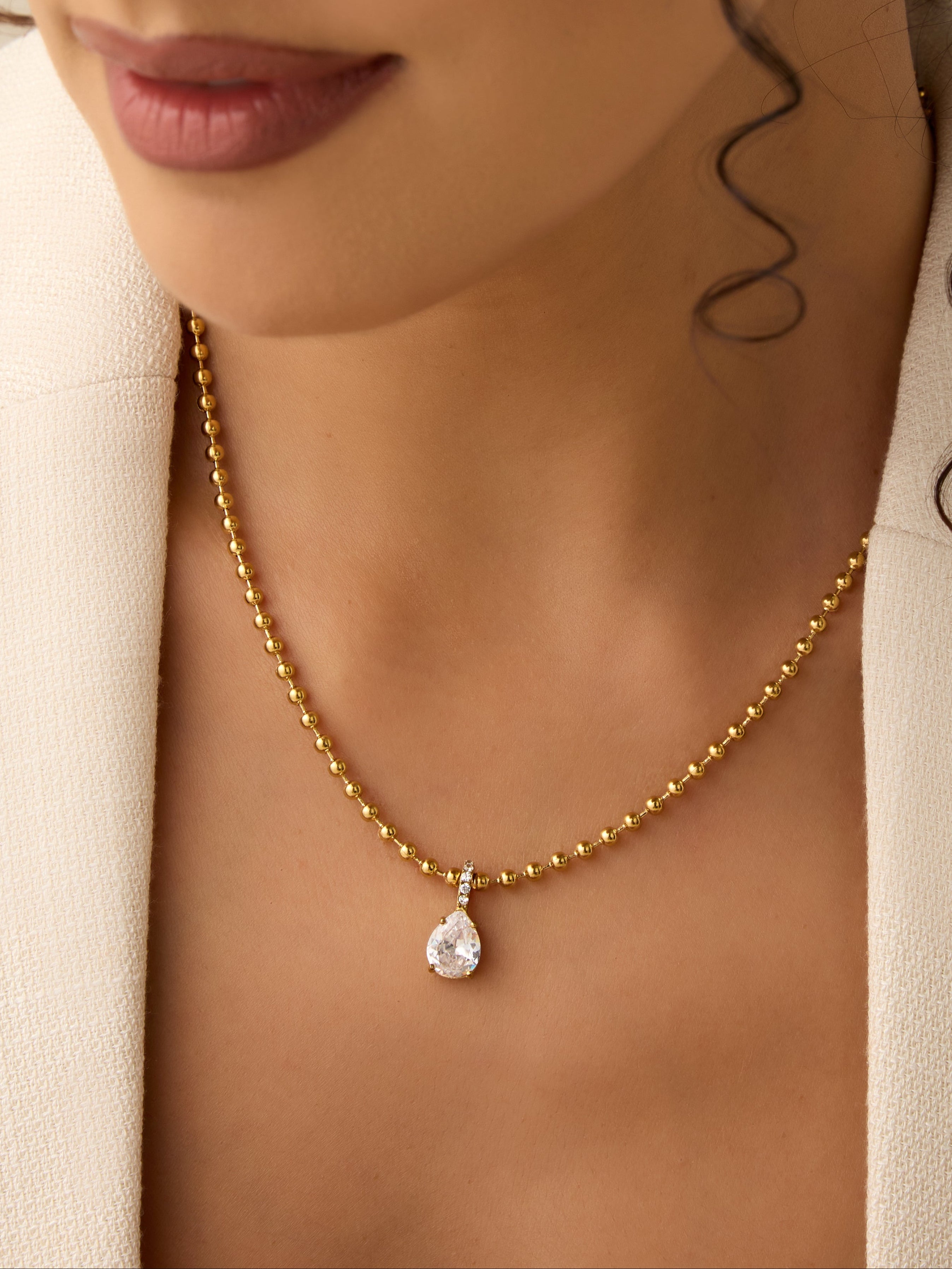 Close-up of a woman wearing a gold necklace with a teardrop pendant.