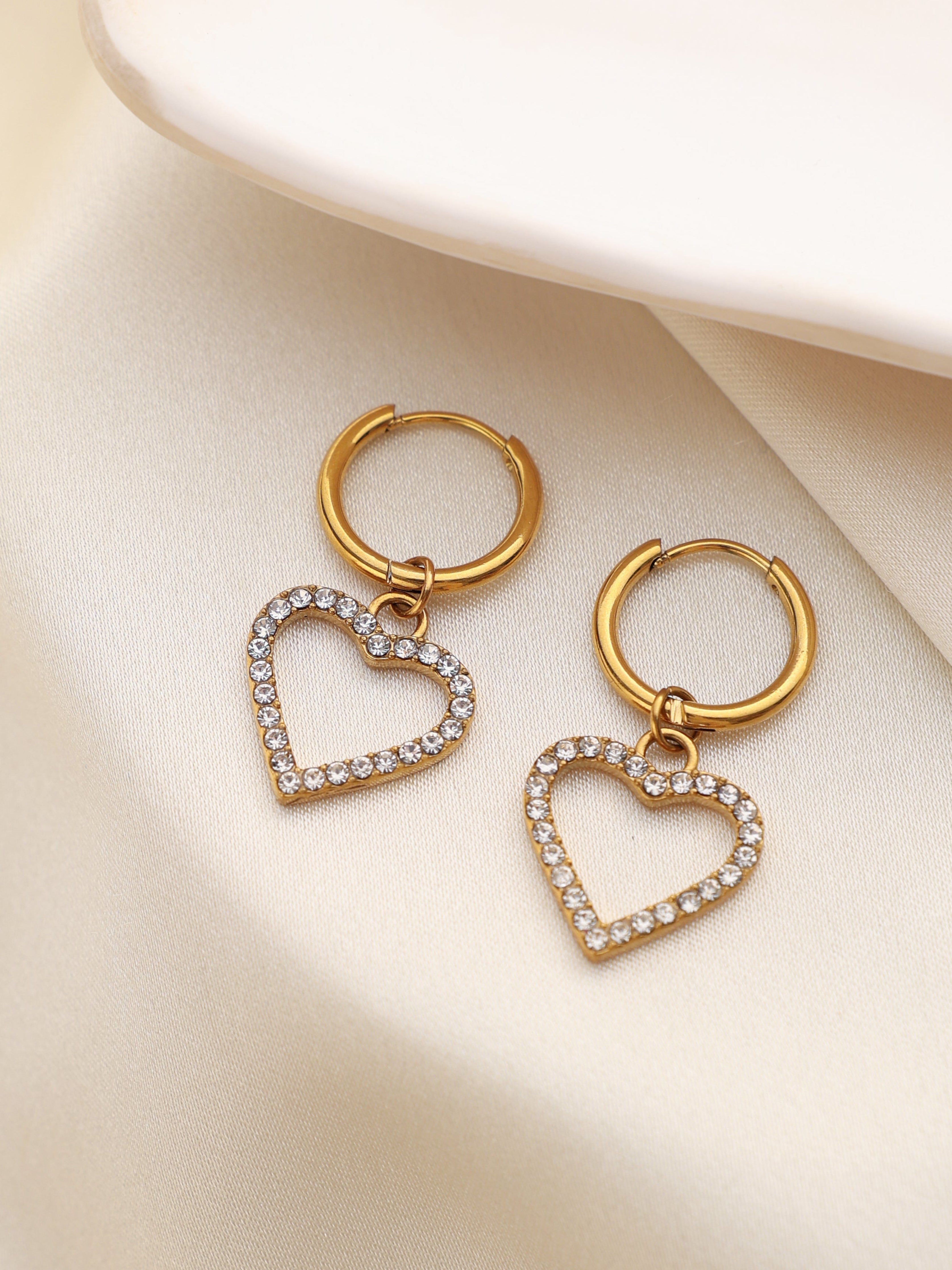 Gold hoop earrings with heart-shaped pendants on a beige surface