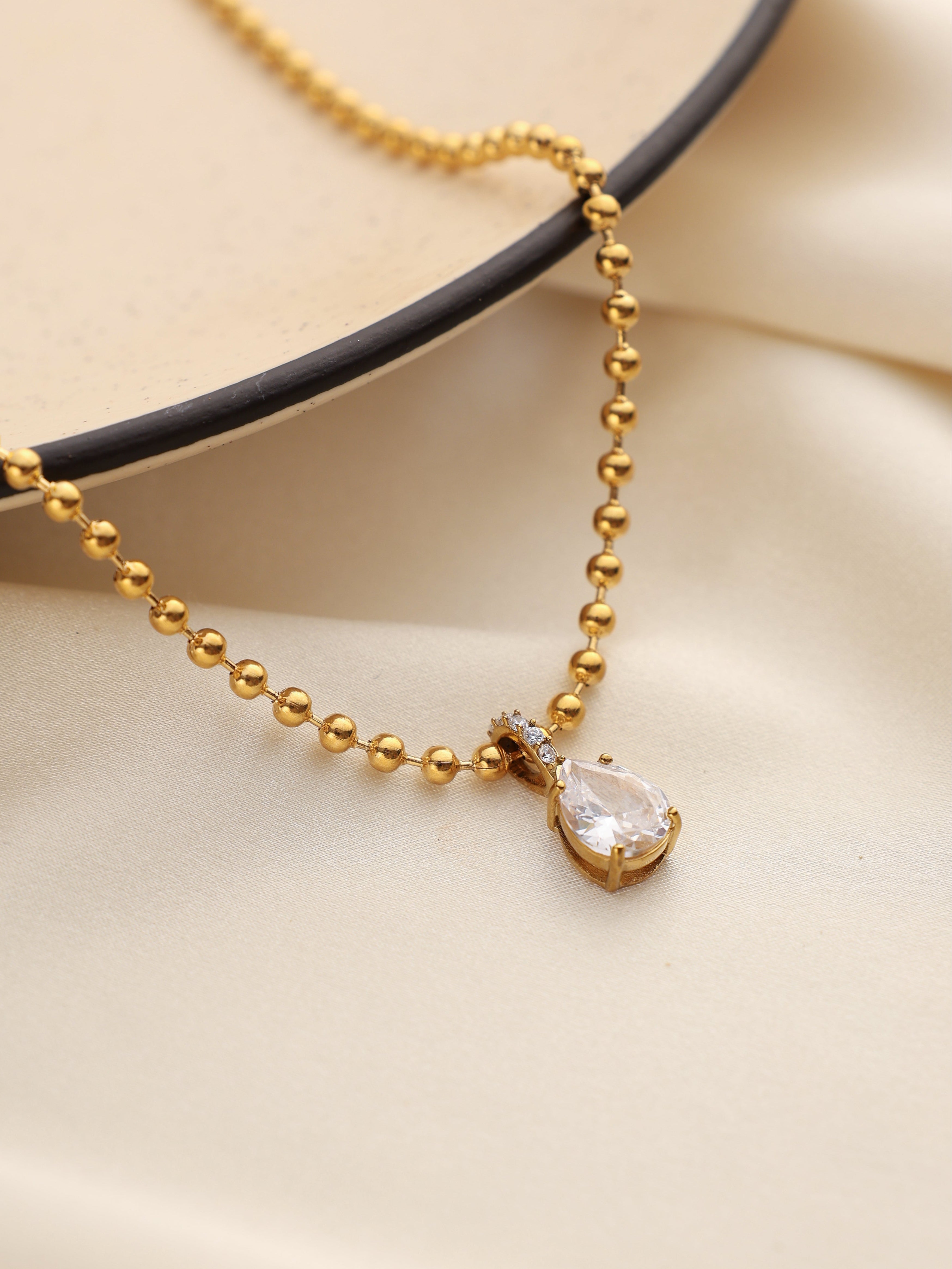 Gold necklace with a teardrop-shaped pendant on a beige background