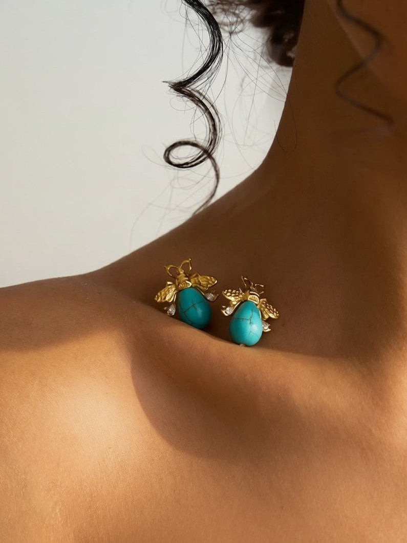 Close-up of a person wearing turquoise earrings with gold accents on a neutral background